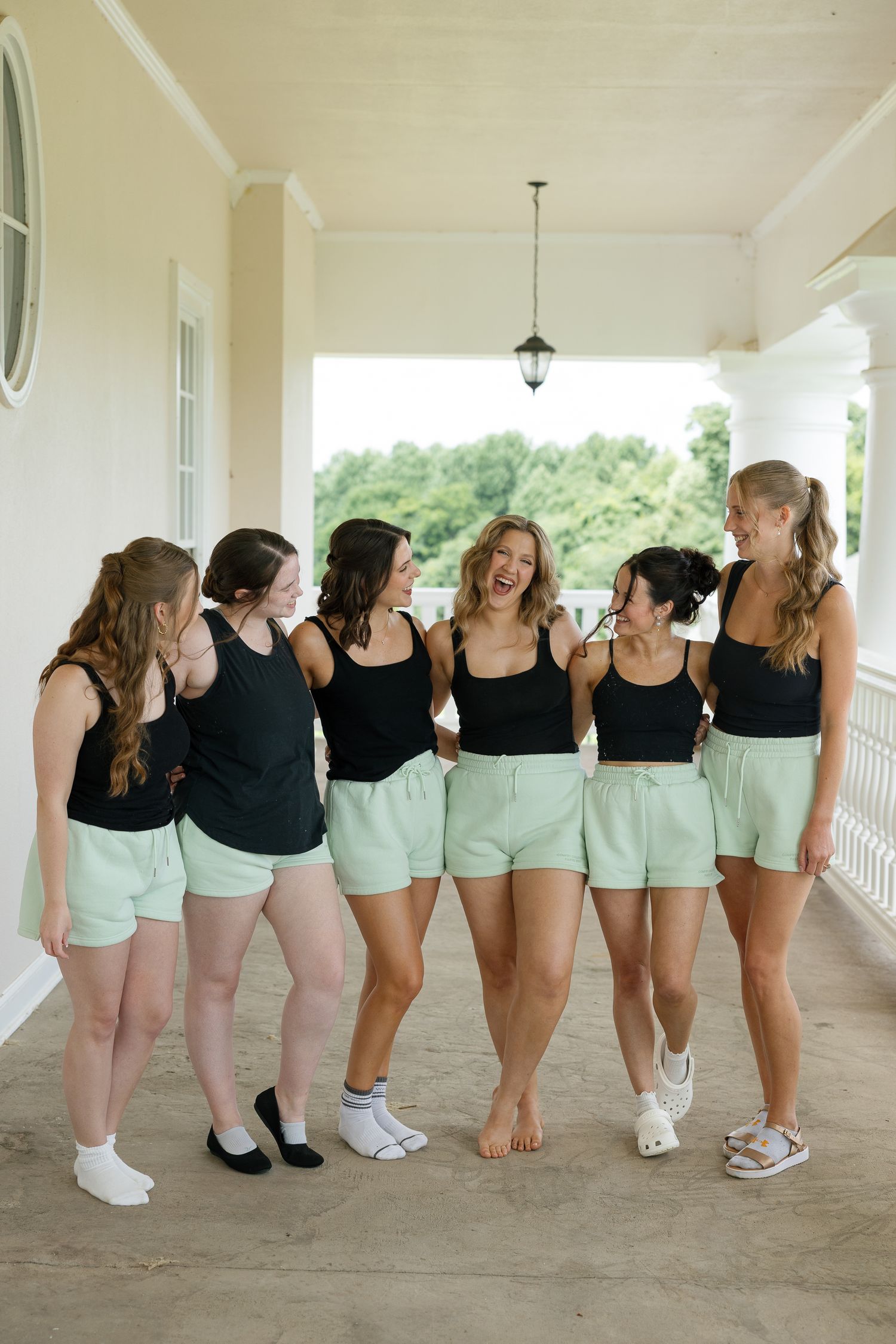 Five women in matching black tops and mint green shorts laughing together on a porch.