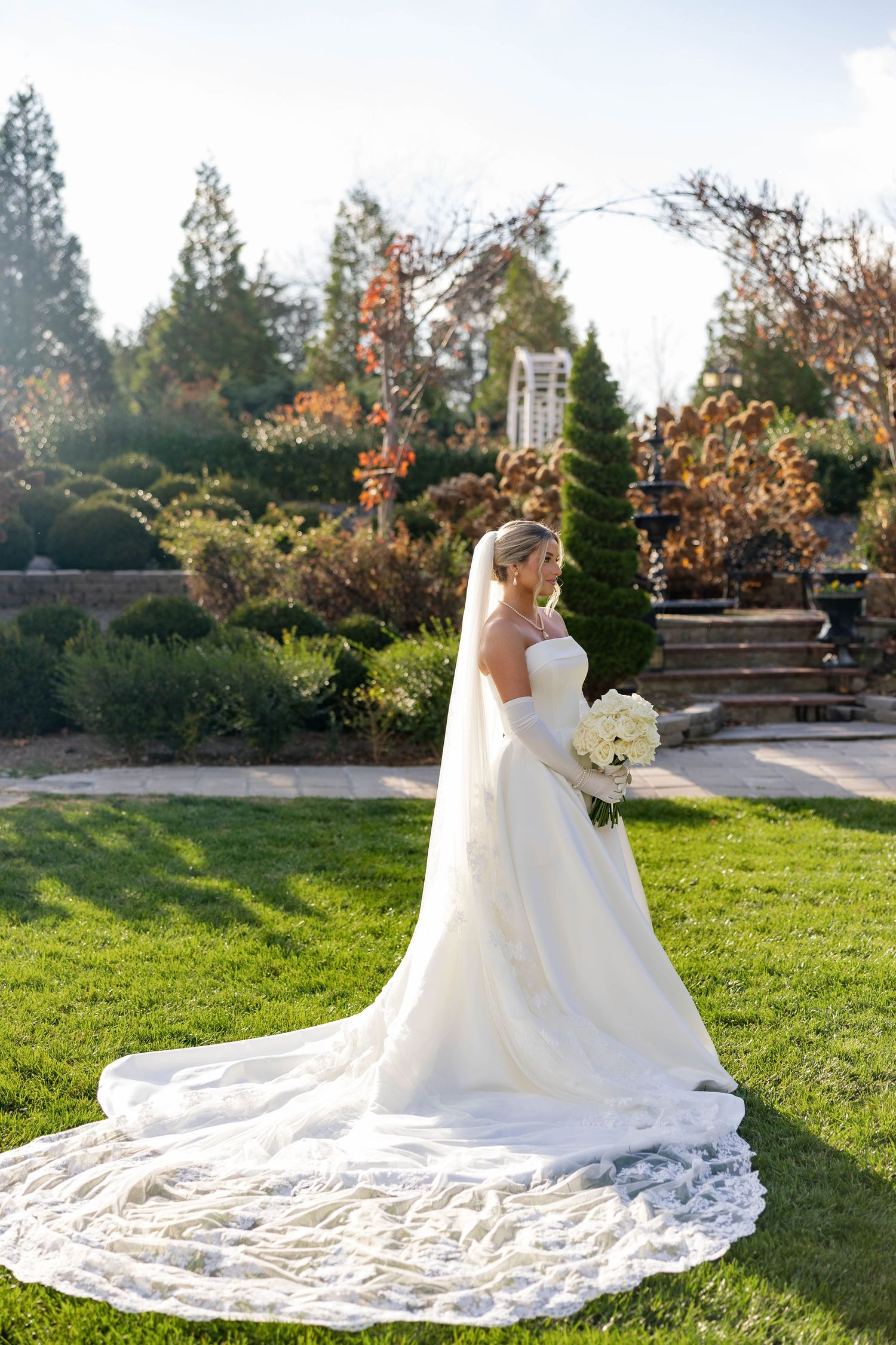 A flowing white wedding dress spreads across green grass in a garden setting.
