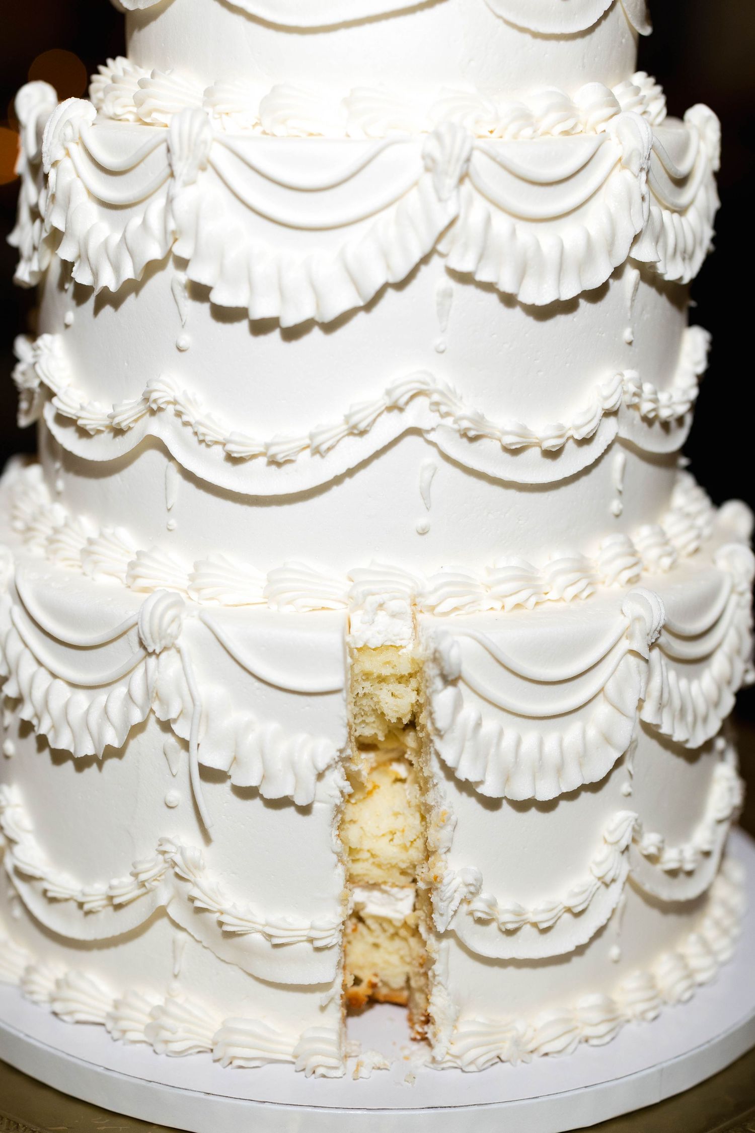 A close-up view of a white tiered wedding cake with classic swag piping designs showing a cut section