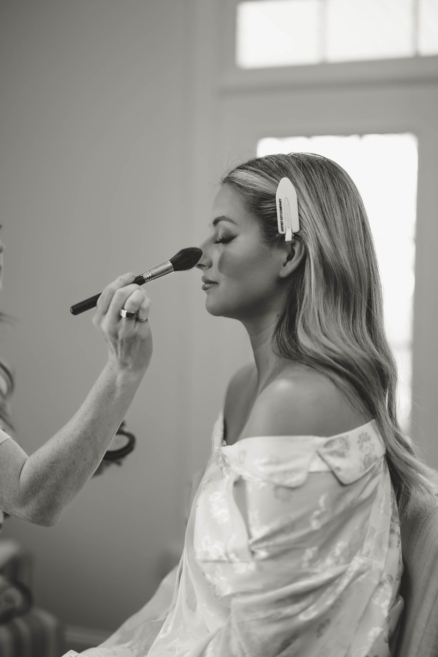 Side view of person in white robe getting makeup applied in natural window light in Kentucky