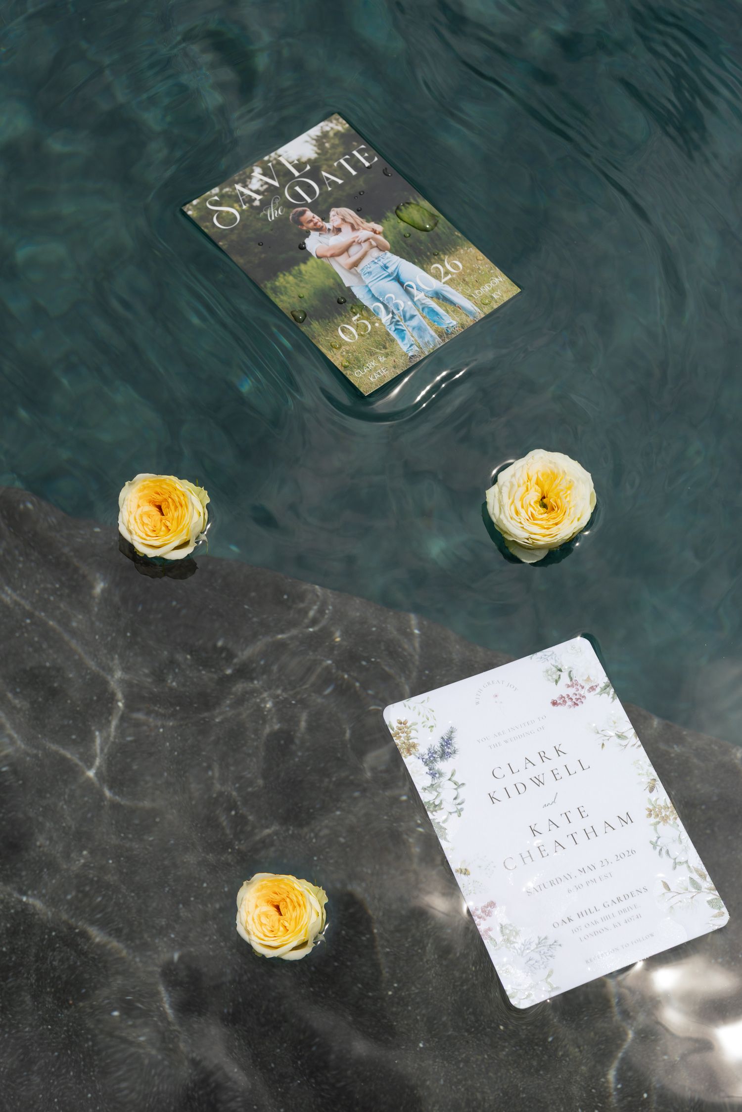 Wedding save the date card floating in water with yellow roses and floral invitation on marble surface.