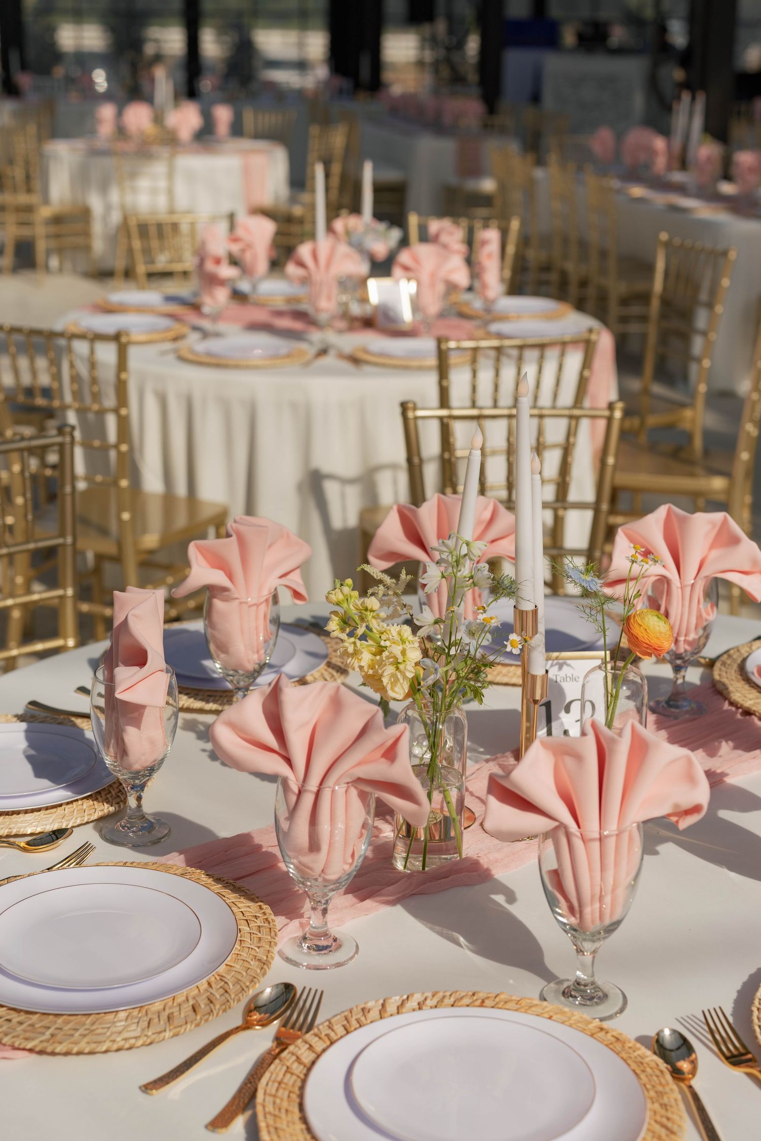 Elegant table settings with pink napkins and gold charger plates at a wedding reception.