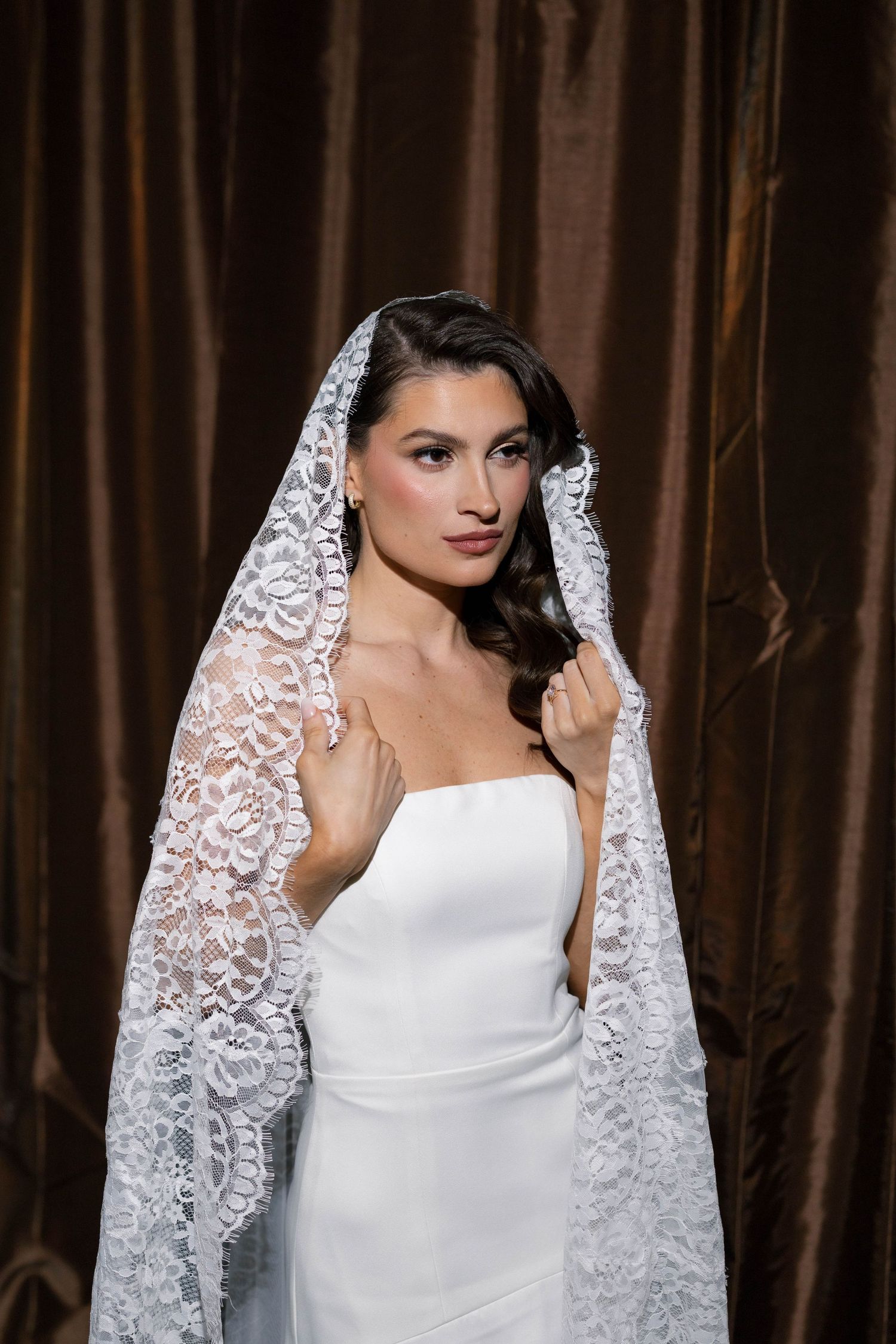 Elegant flash bridal portrait with white lace veil against brown curtain backdrop.