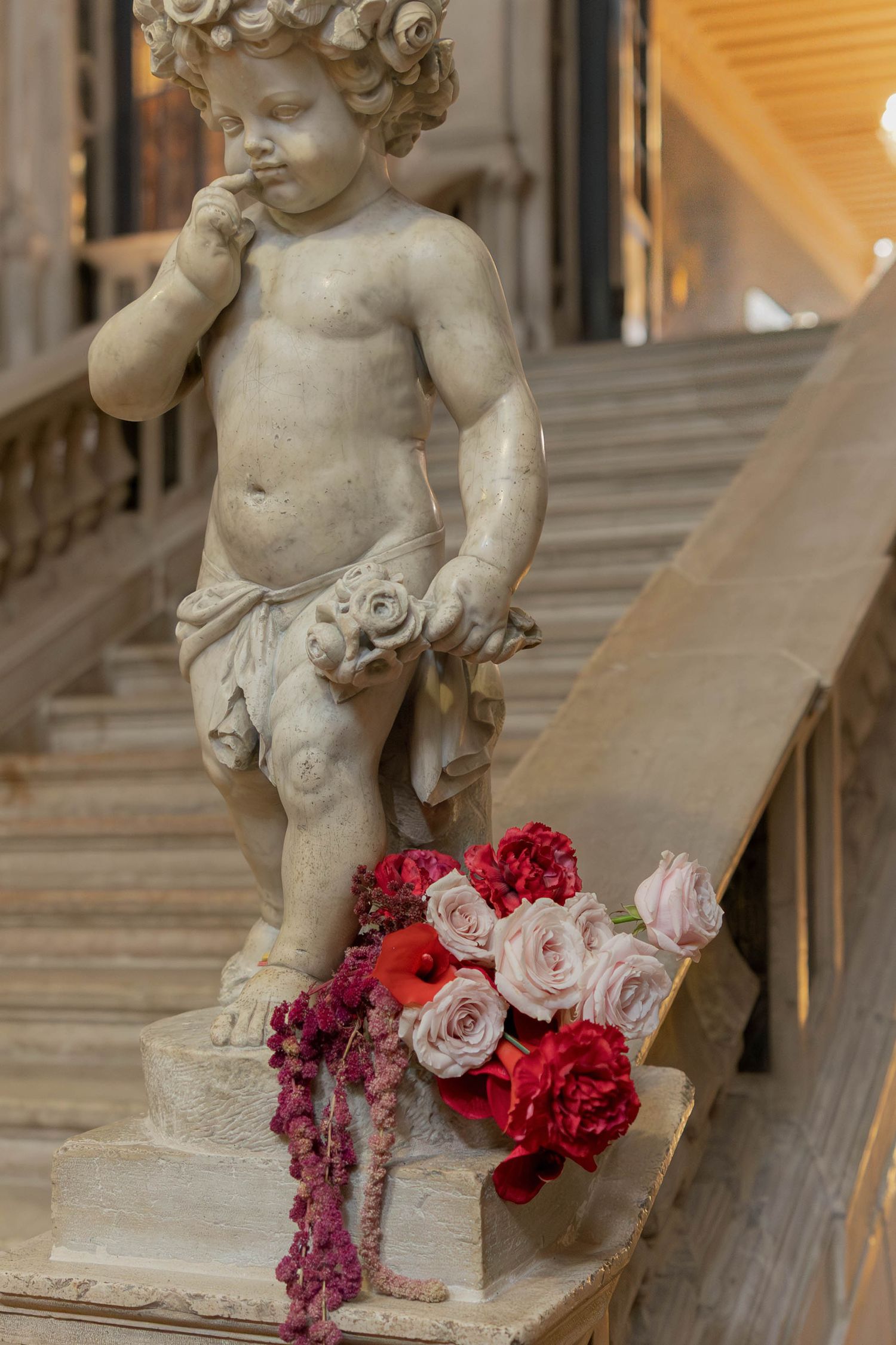 Stone cherub statue decorates elegant staircase with pink and red roses in Venice Italy