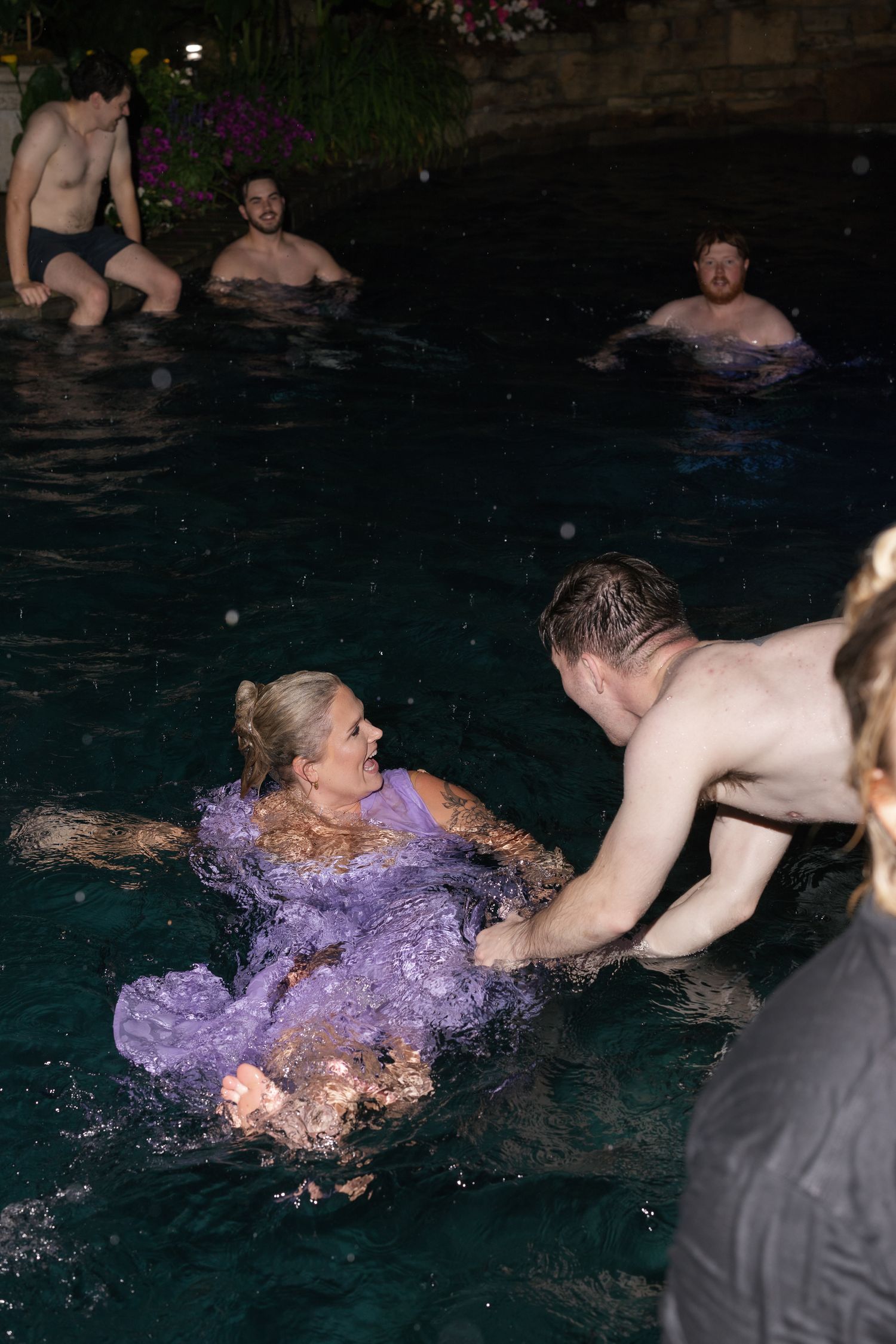Woman in purple dress splashing in pool at night surrounded by people in water.
