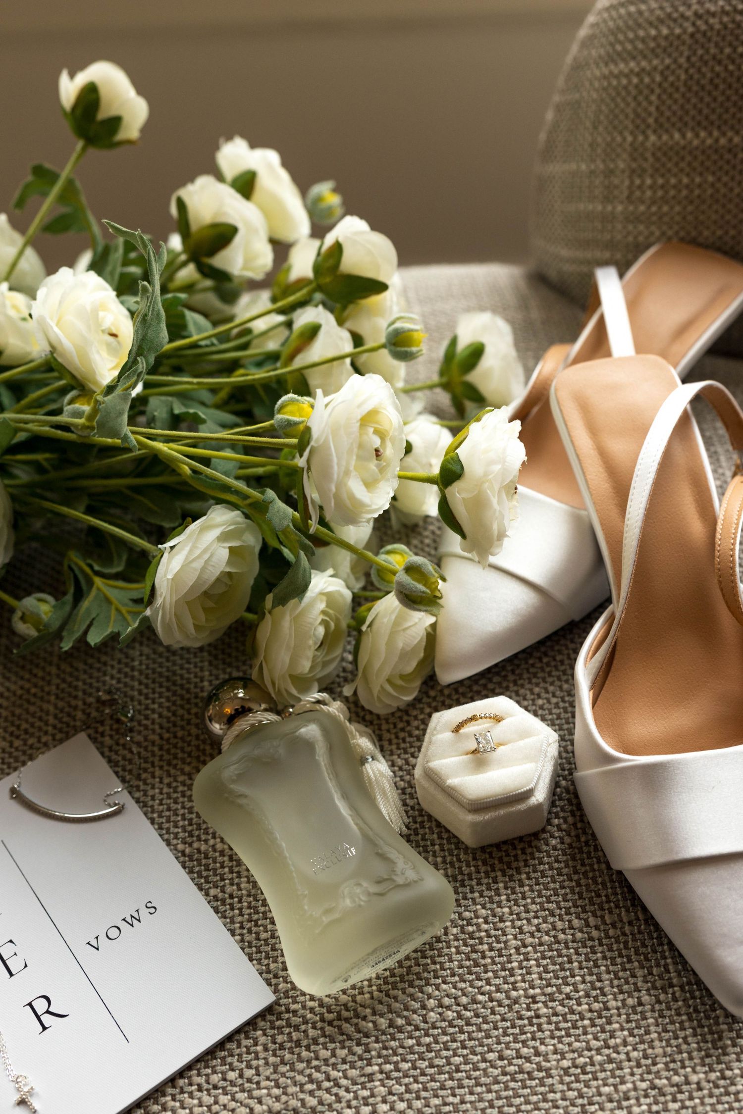White roses and bridal shoes arranged with vow cards on textured surface.