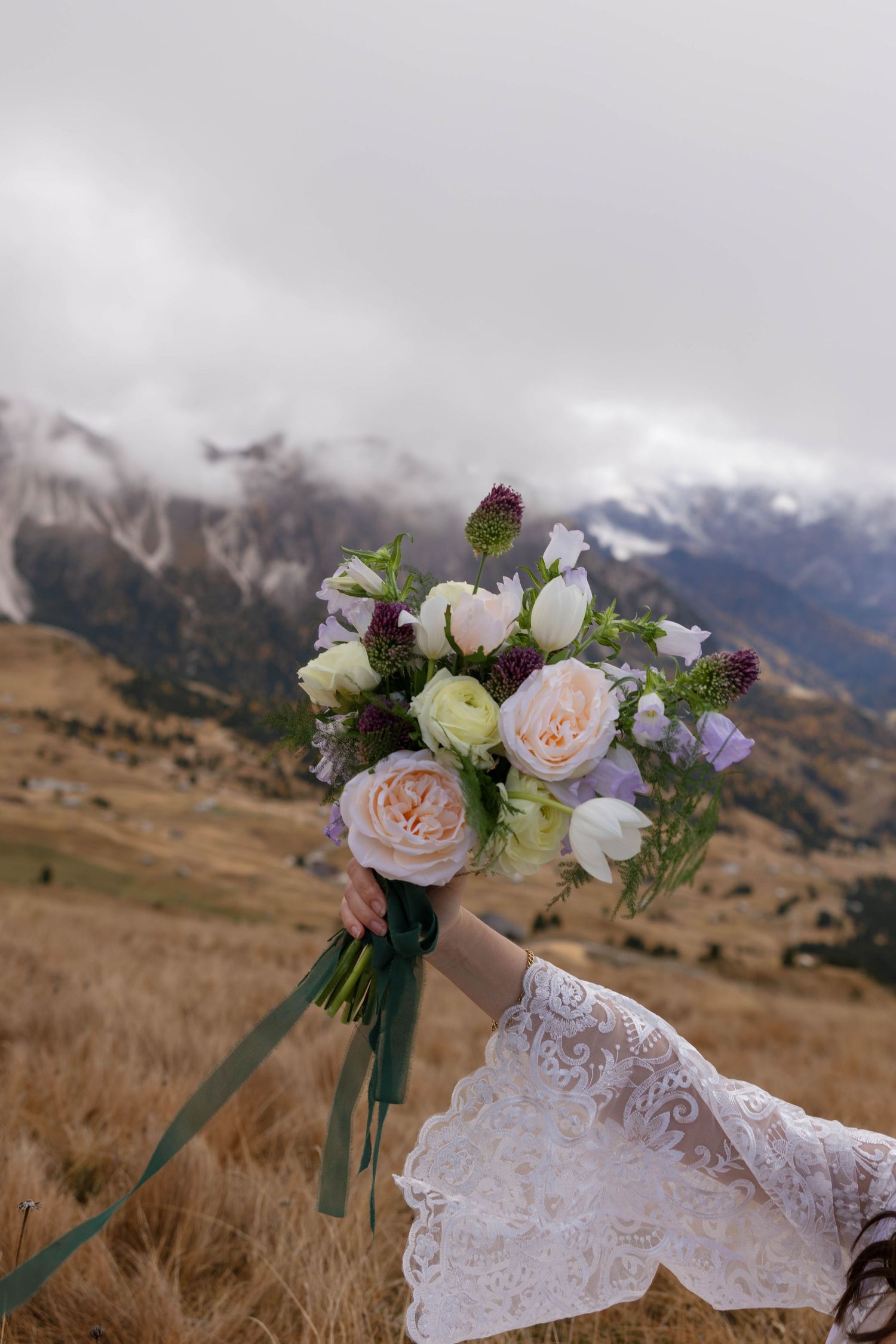Wedding bouquet with pink and white roses against mountain landscape backdrop.