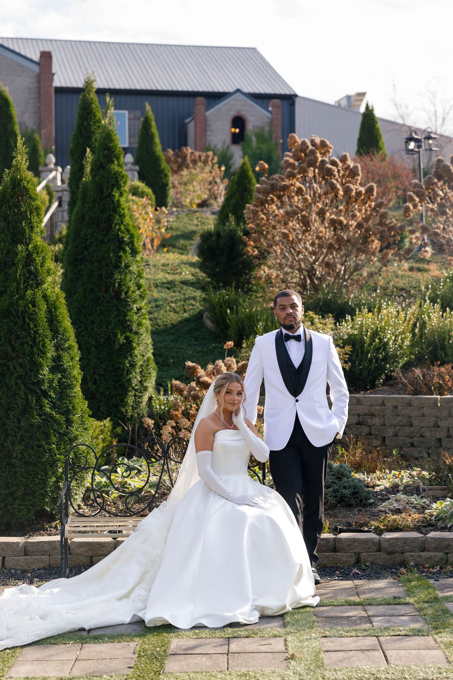 Elegant wedding couple posing in formal attire on garden stone patio.