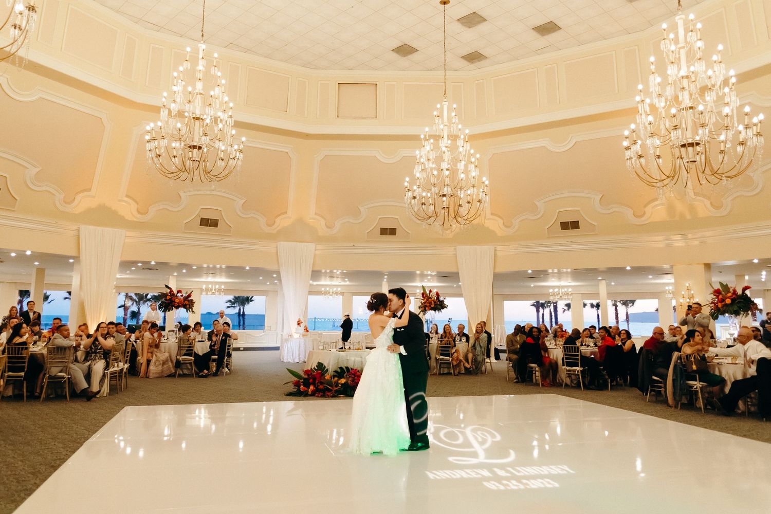 Couples first dance in grand ballroom with ornate chandeliers and circular dance floor.