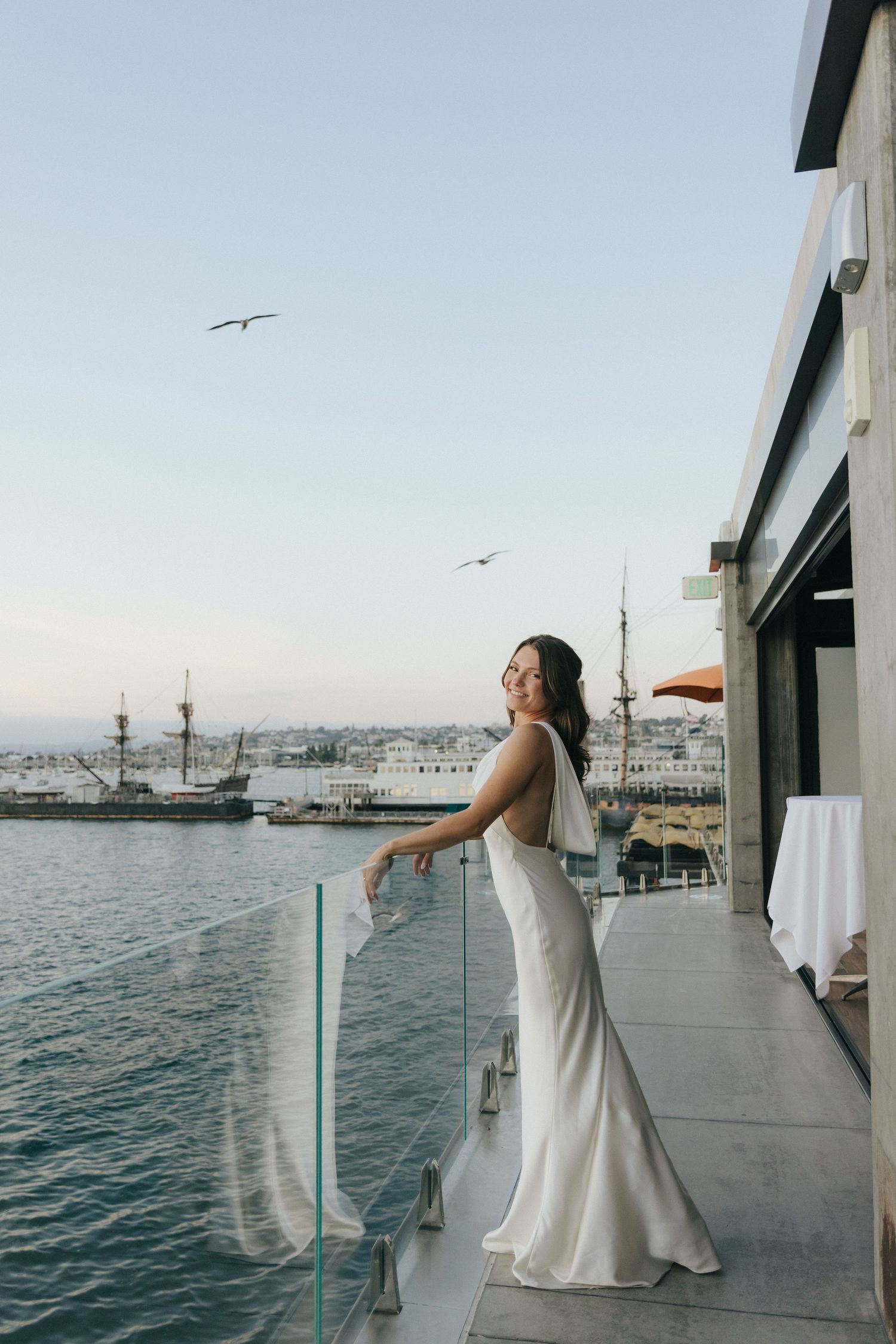 A sequence of photos showing someone in a white wedding dress posing on a waterfront deck with boats in the harbor.