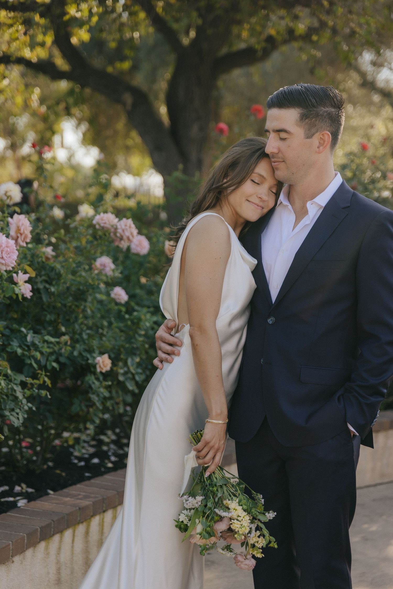 A romantic couple embraces in a garden setting with blooming roses, captured in a series of intimate wedding photos.