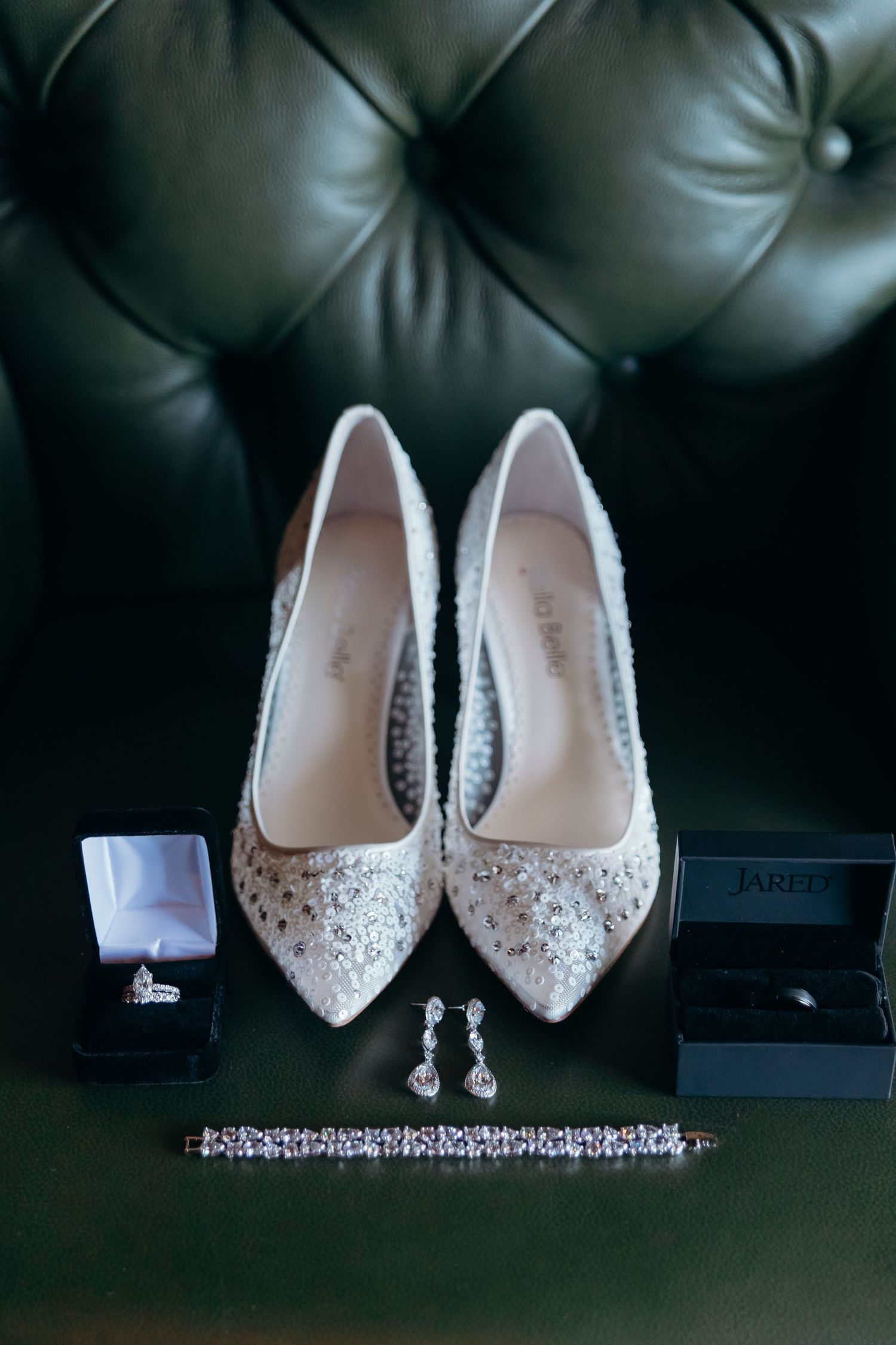 Elegant beaded wedding shoes displayed with sparkly jewelry and accessories on a dark leather surface.