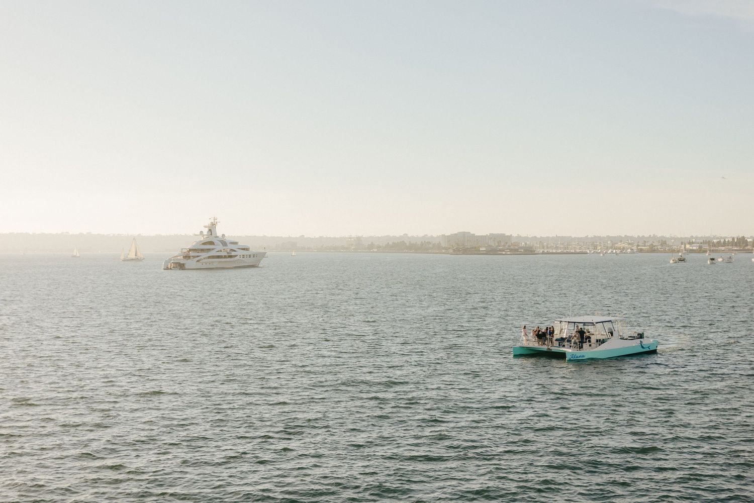 A series of boats and vessels navigate across calm blue waters with distant shoreline visible in the background.