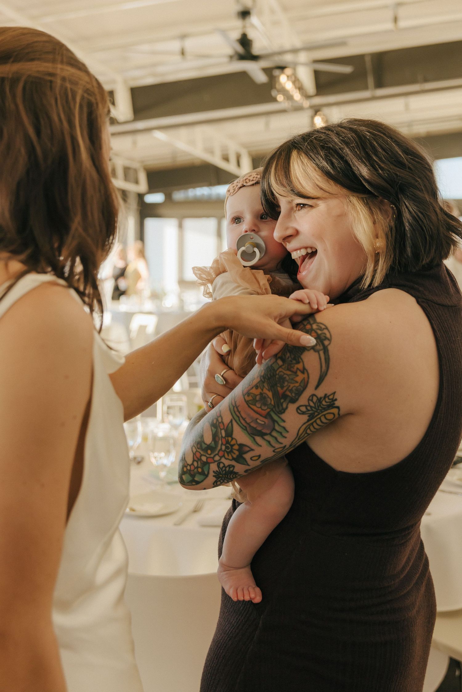 A joyful moment at a wedding reception as guests share laughter while holding a small baby.