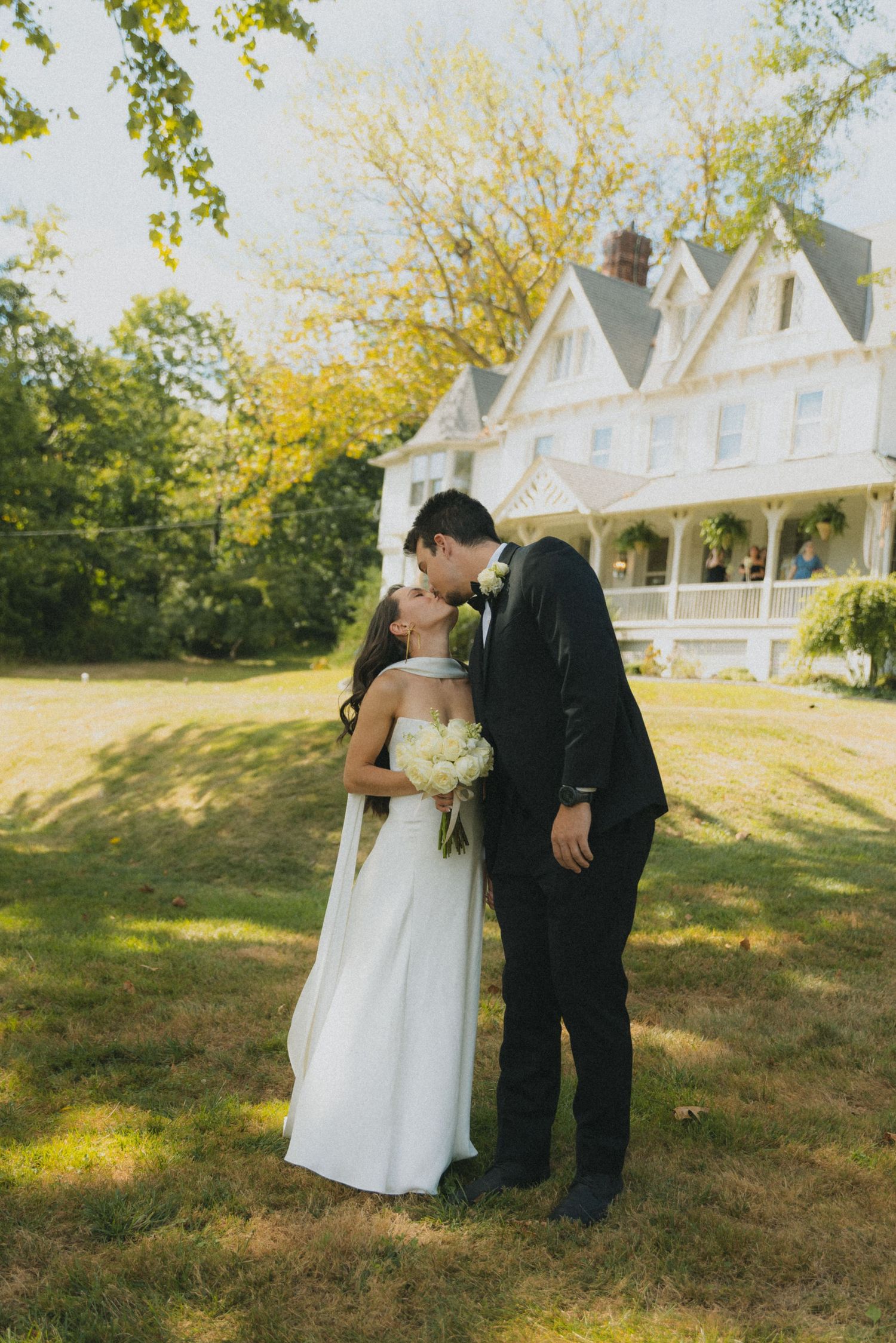 A couple shares intimate wedding moments on the lawn of a white Victorian-style house.