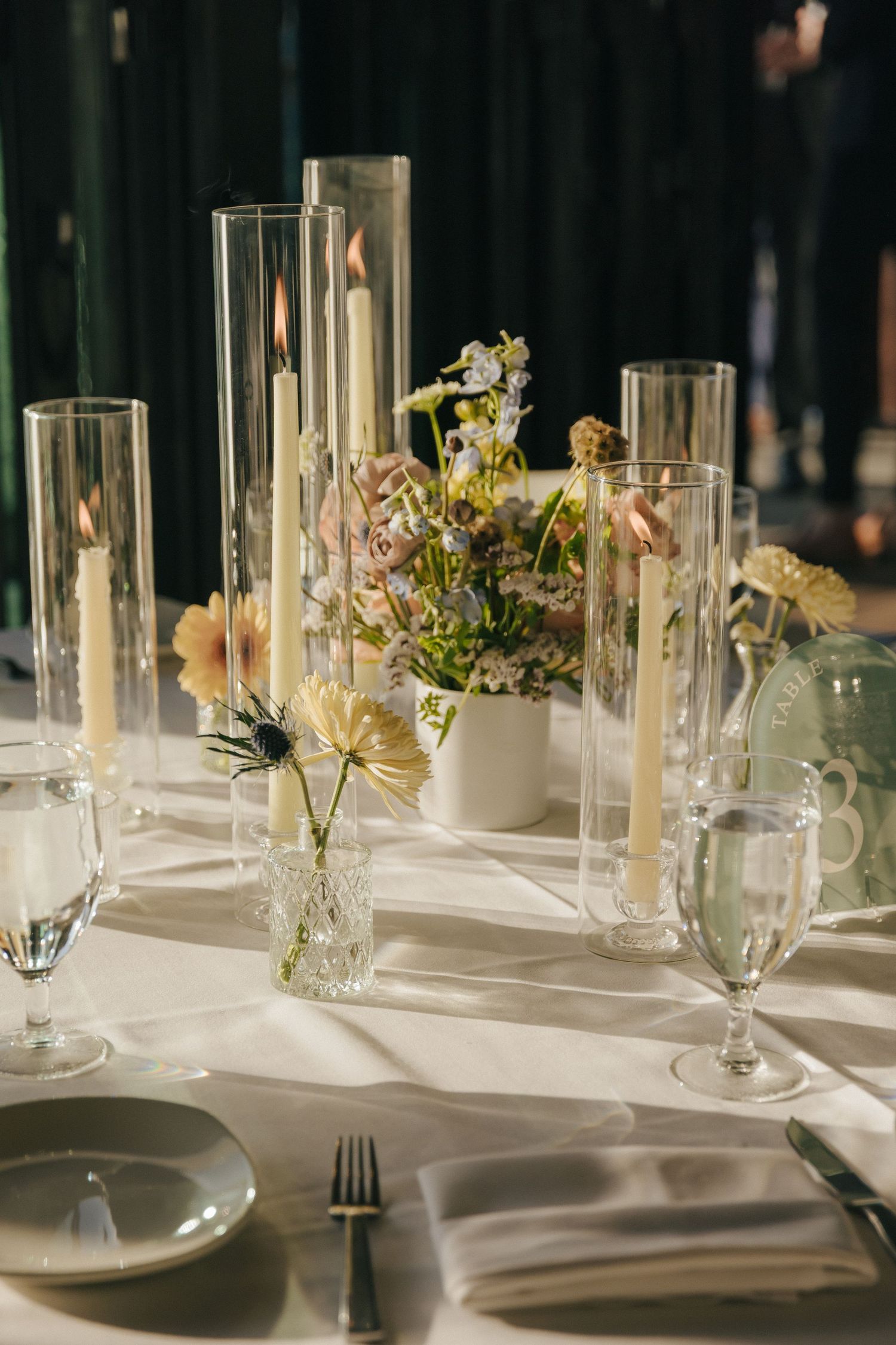 Elegant wedding table setting with glass vases, delicate flowers and white tablecloth in natural light.