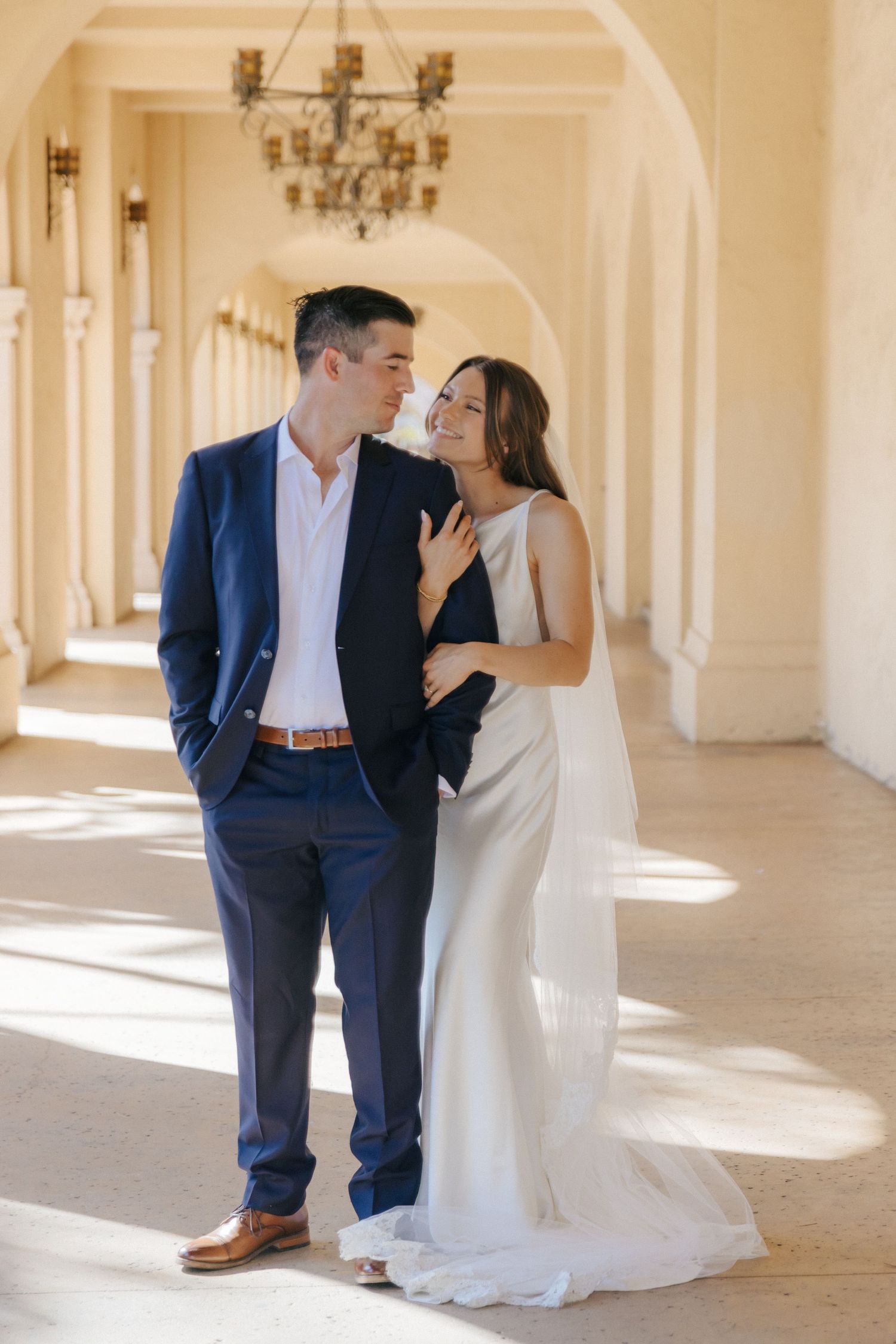 A couple shares intimate moments in an elegant hallway with arched windows and natural light.