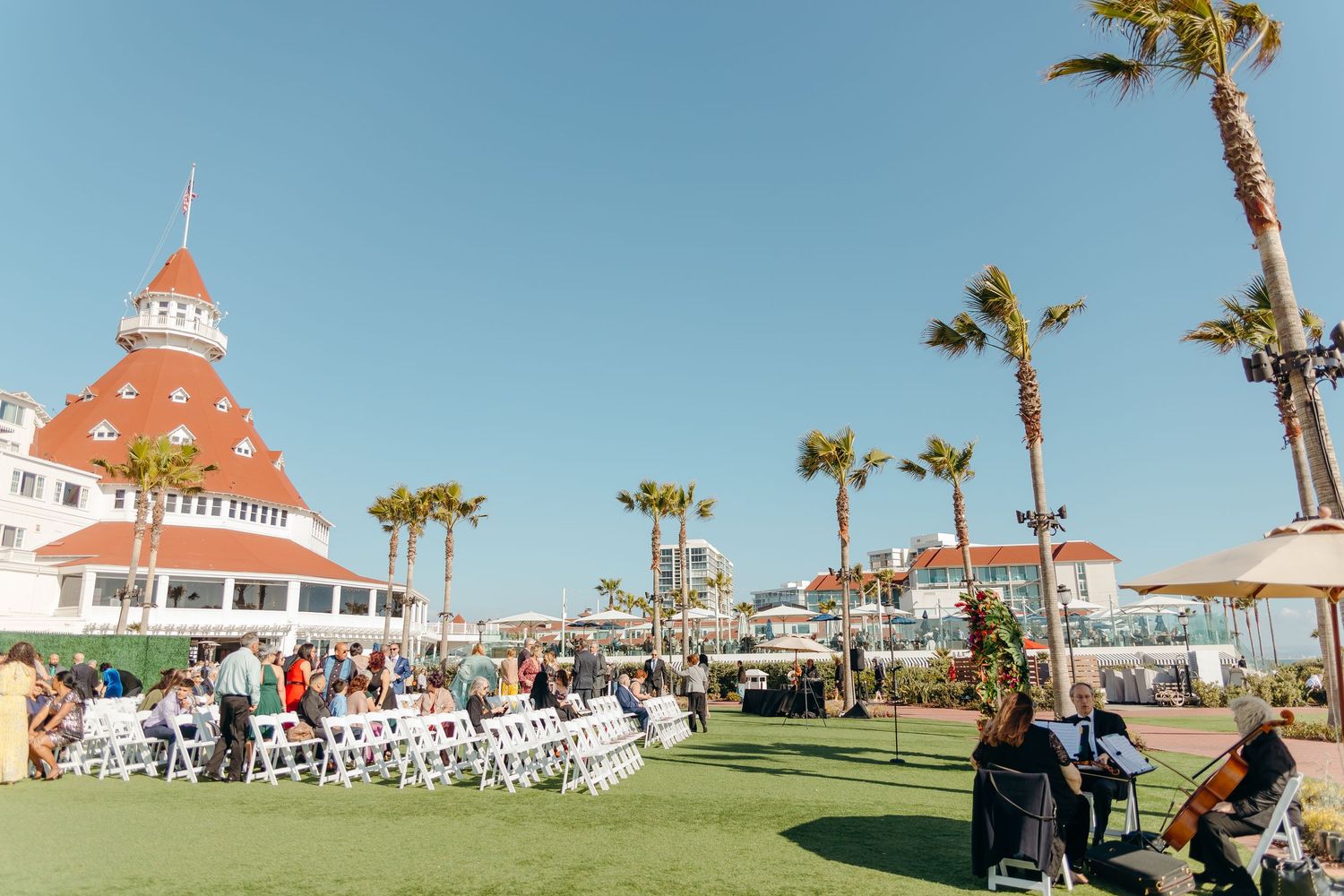 Hotel Del Coronado's iconic red turret and palm trees frame an outdoor wedding ceremony setup.