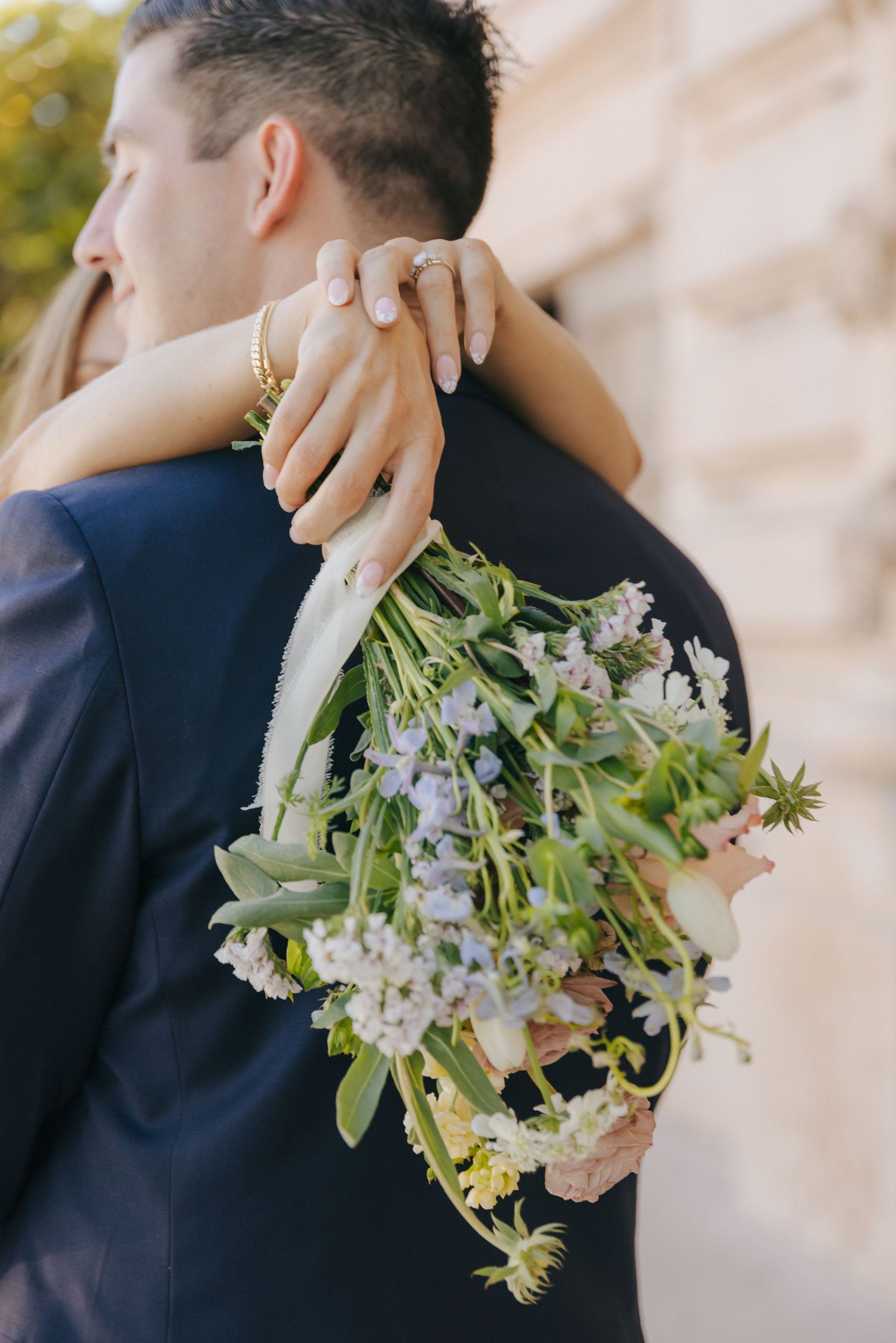 Close-up of embracing couple at wedding with white floral bouquet and navy suit visible.