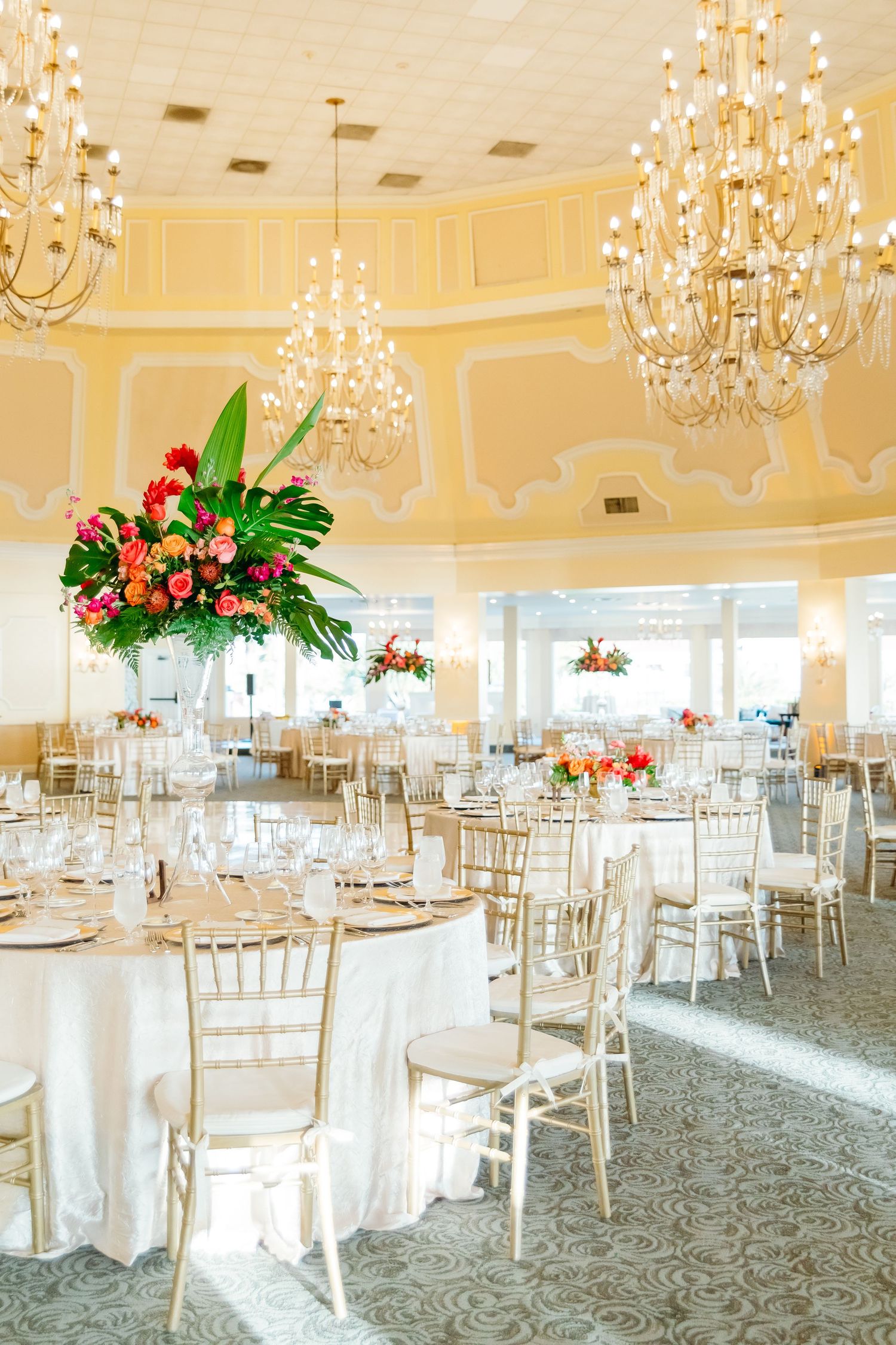 Elegant ballroom reception venue with crystal chandeliers and tropical floral centerpieces.