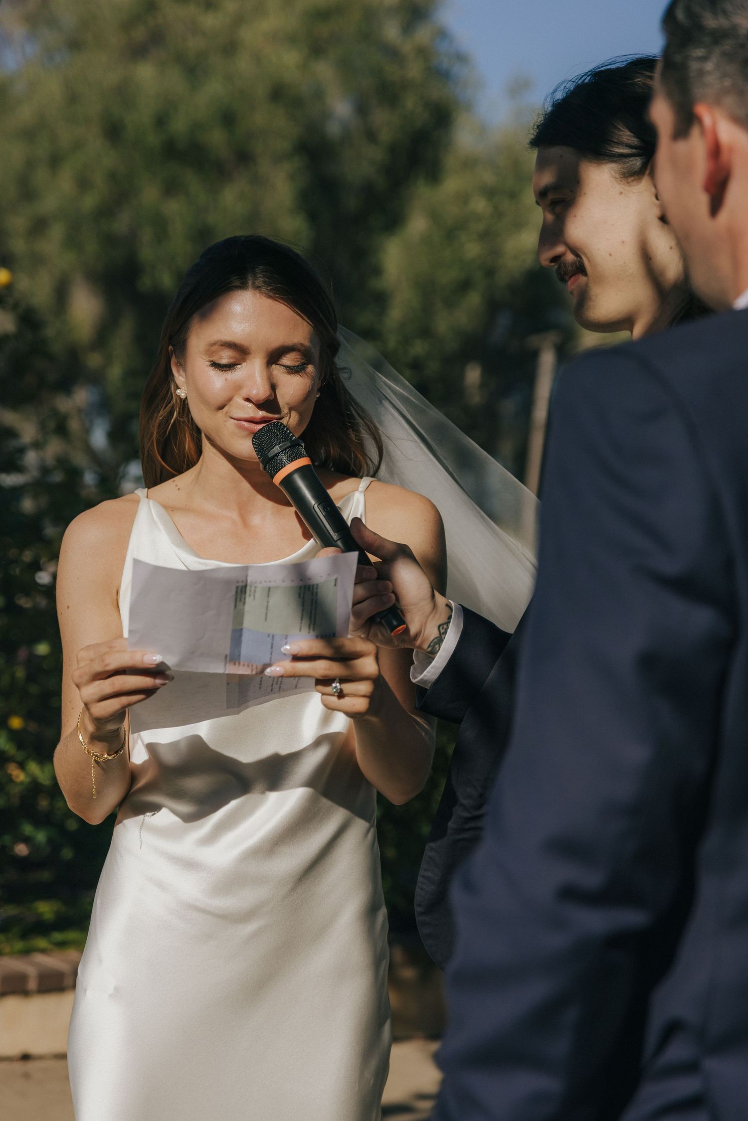 A couple shares an intimate moment while reading handwritten letters during an outdoor wedding ceremony.