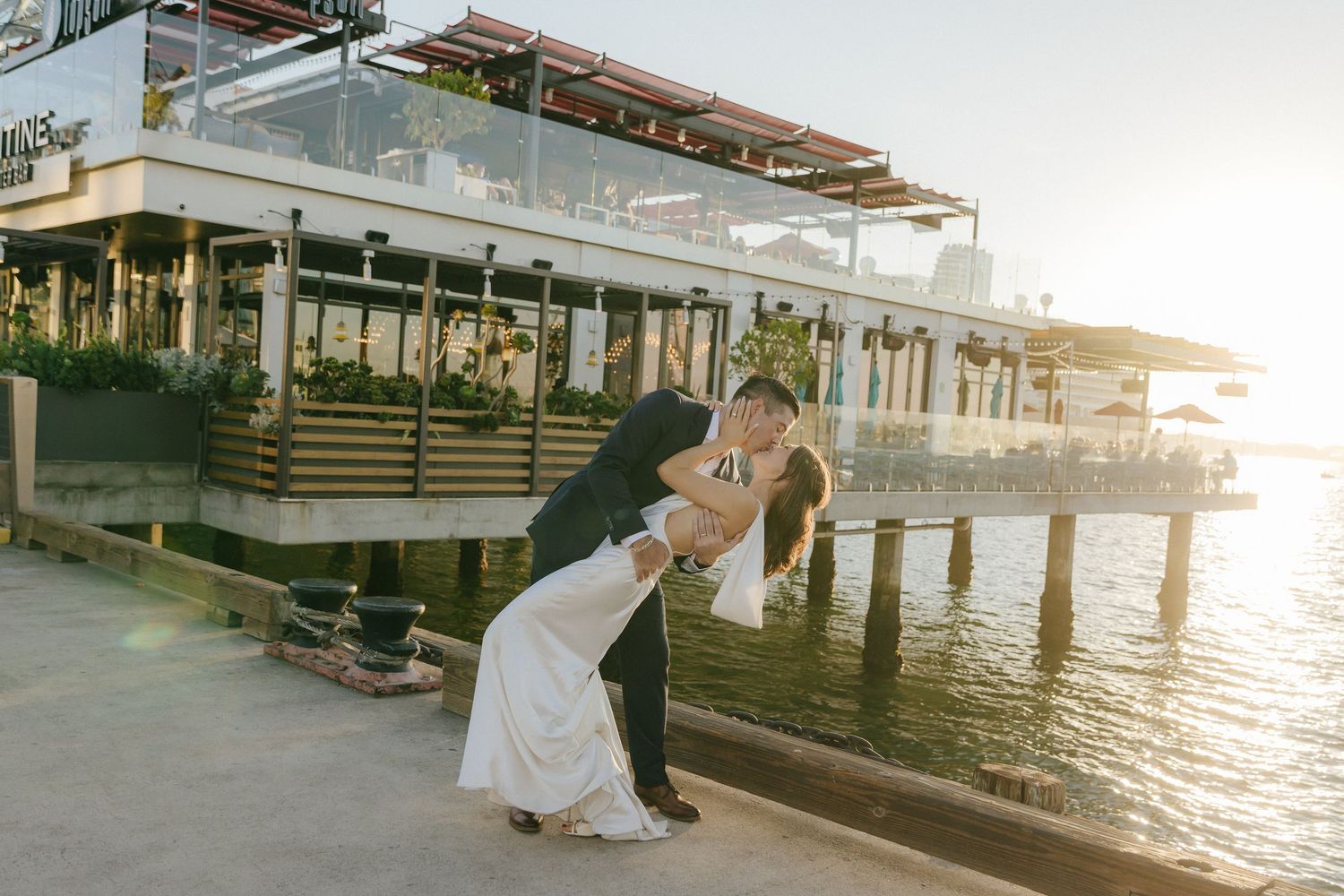 Romantic couple shares intimate moments at sunset on a wooden pier by the waterfront.