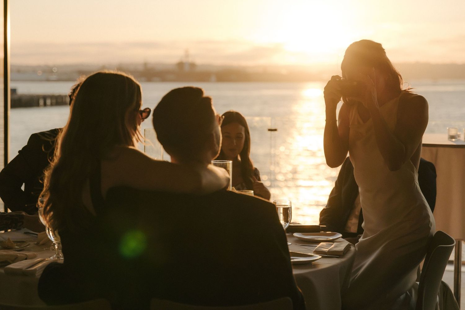 Silhouetted people gathered at sunset by the ocean with warm golden light reflecting off the water.