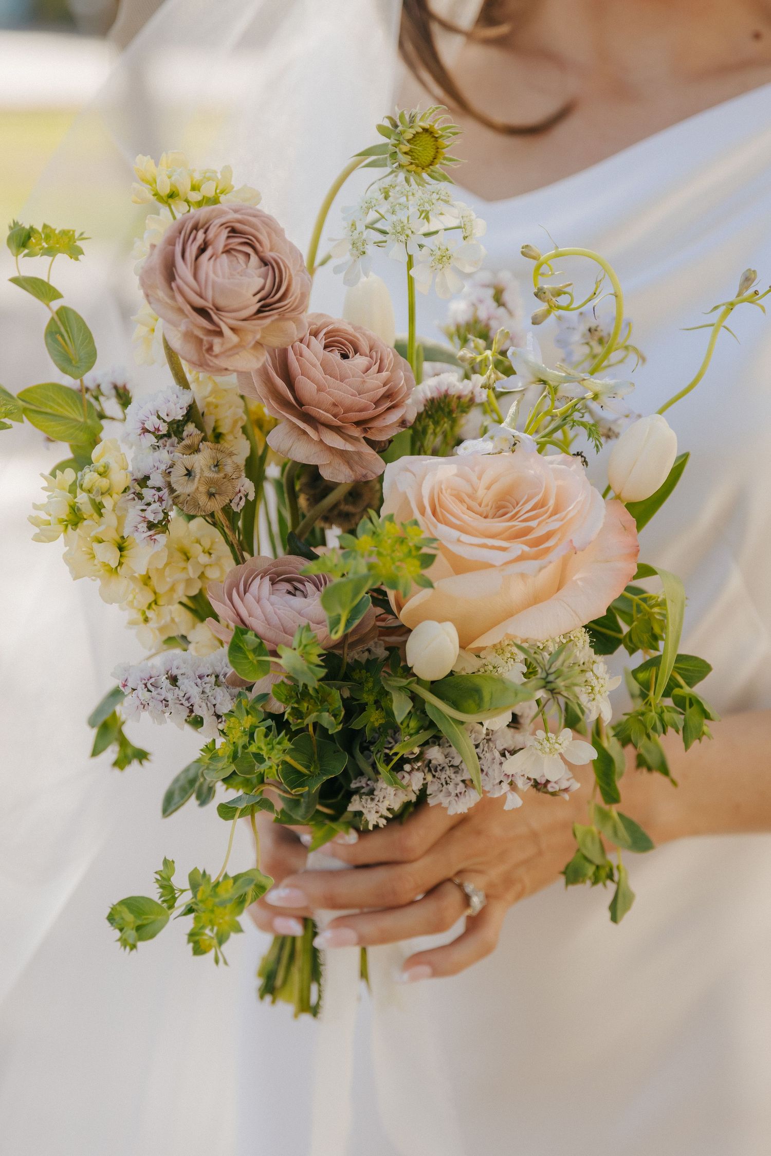 Delicate bridal bouquet featuring blush roses, ranunculus and wildflowers in a romantic garden style.