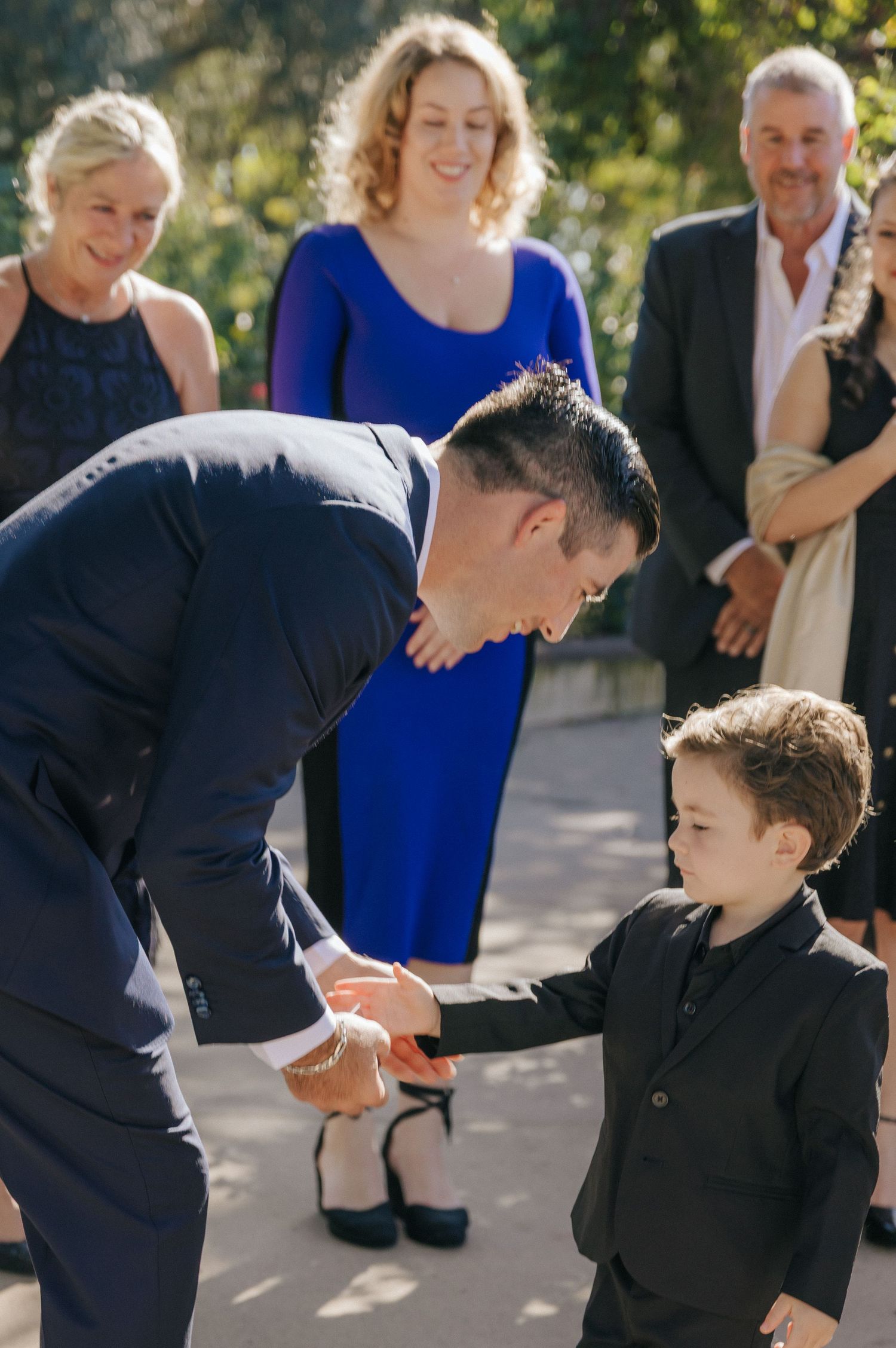 A candid sequence of a child and adult in formal attire sharing a playful moment at an outdoor event.