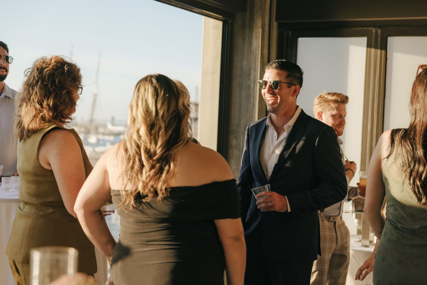 A group of people socializing and mingling at an indoor event with natural lighting streaming through windows.