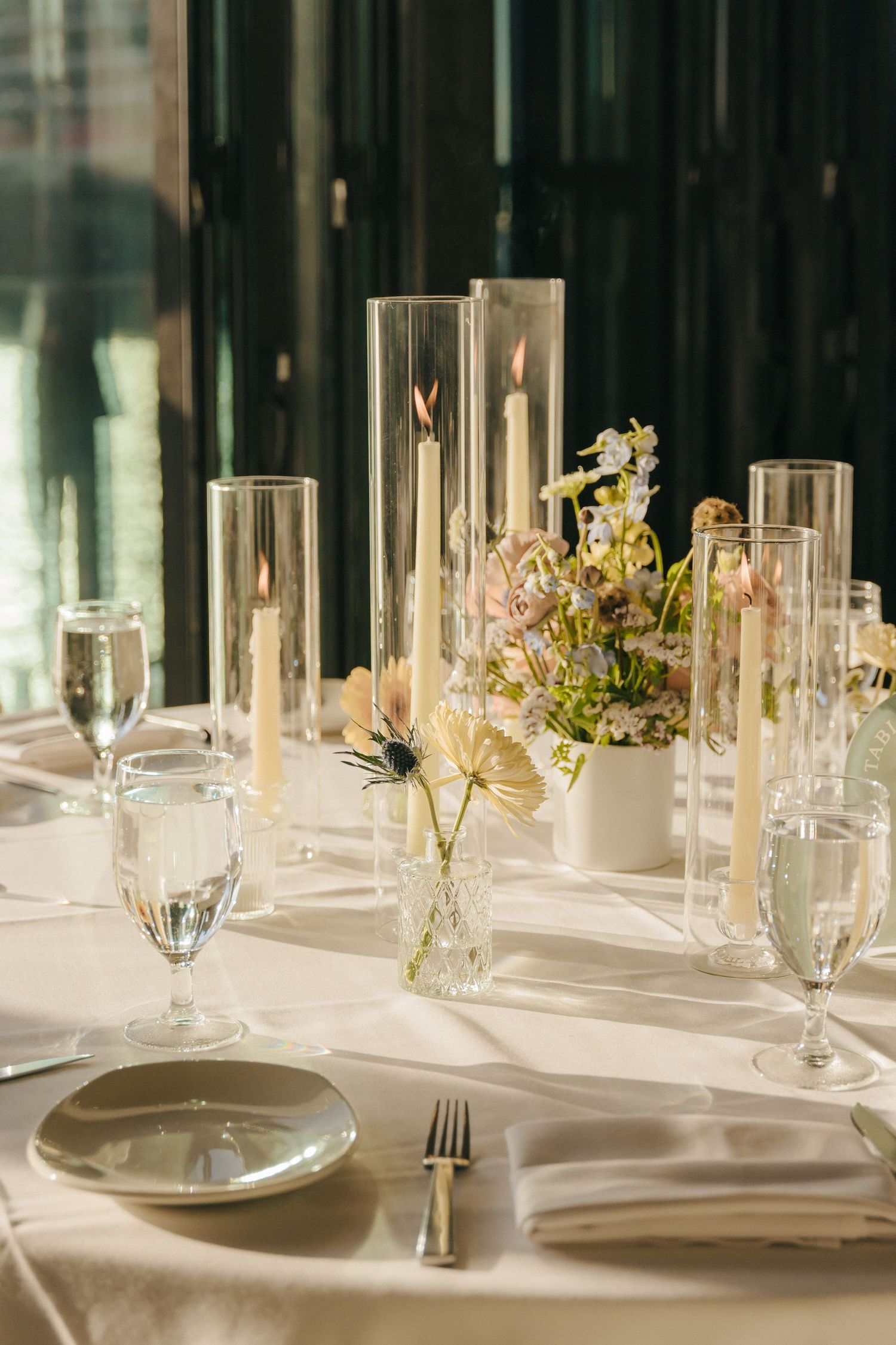 Elegant table settings with white linens, glass candleholders, and delicate floral arrangements at a formal dining event.
