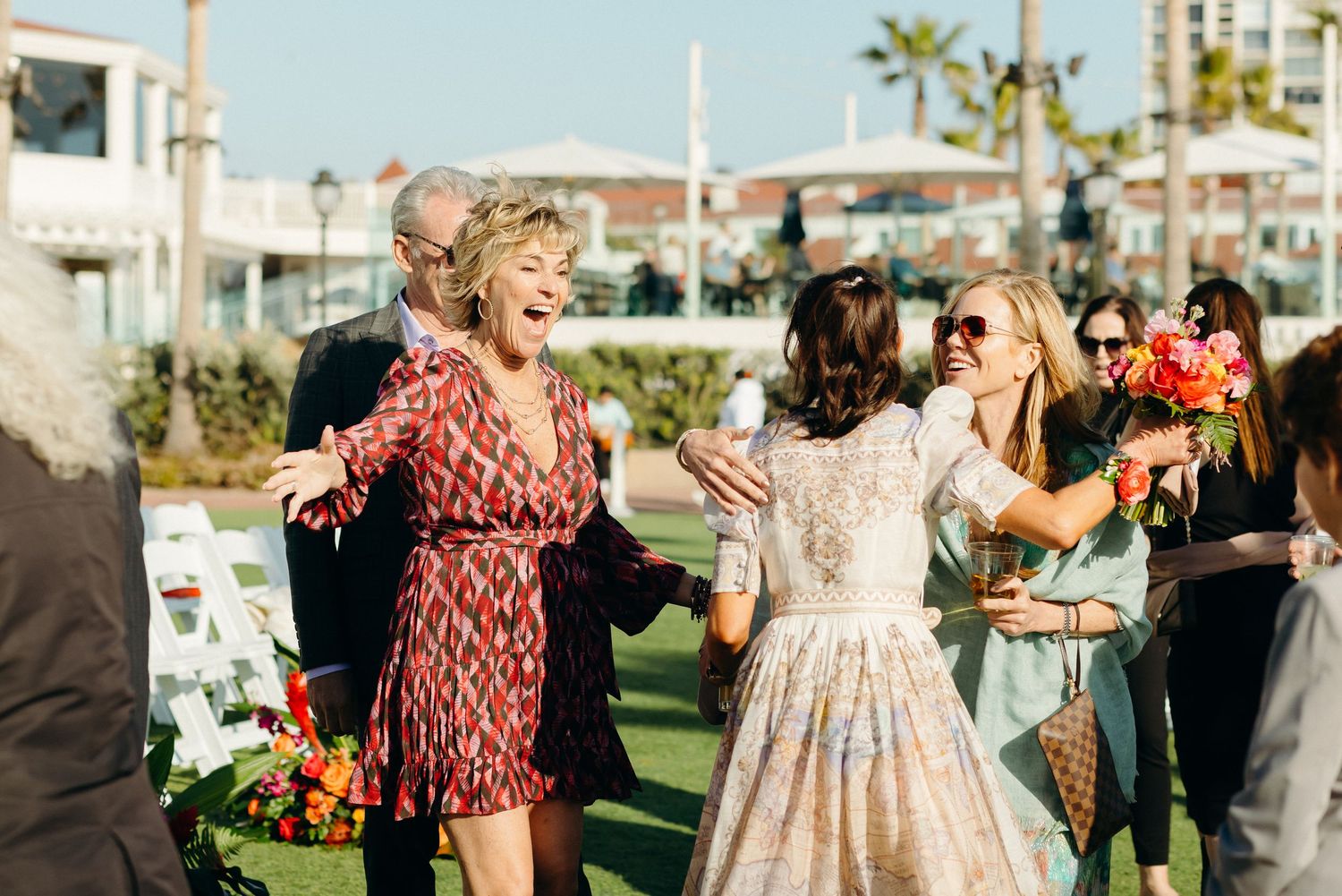 Joyful wedding celebration with guests dancing outdoors on a sunny day.