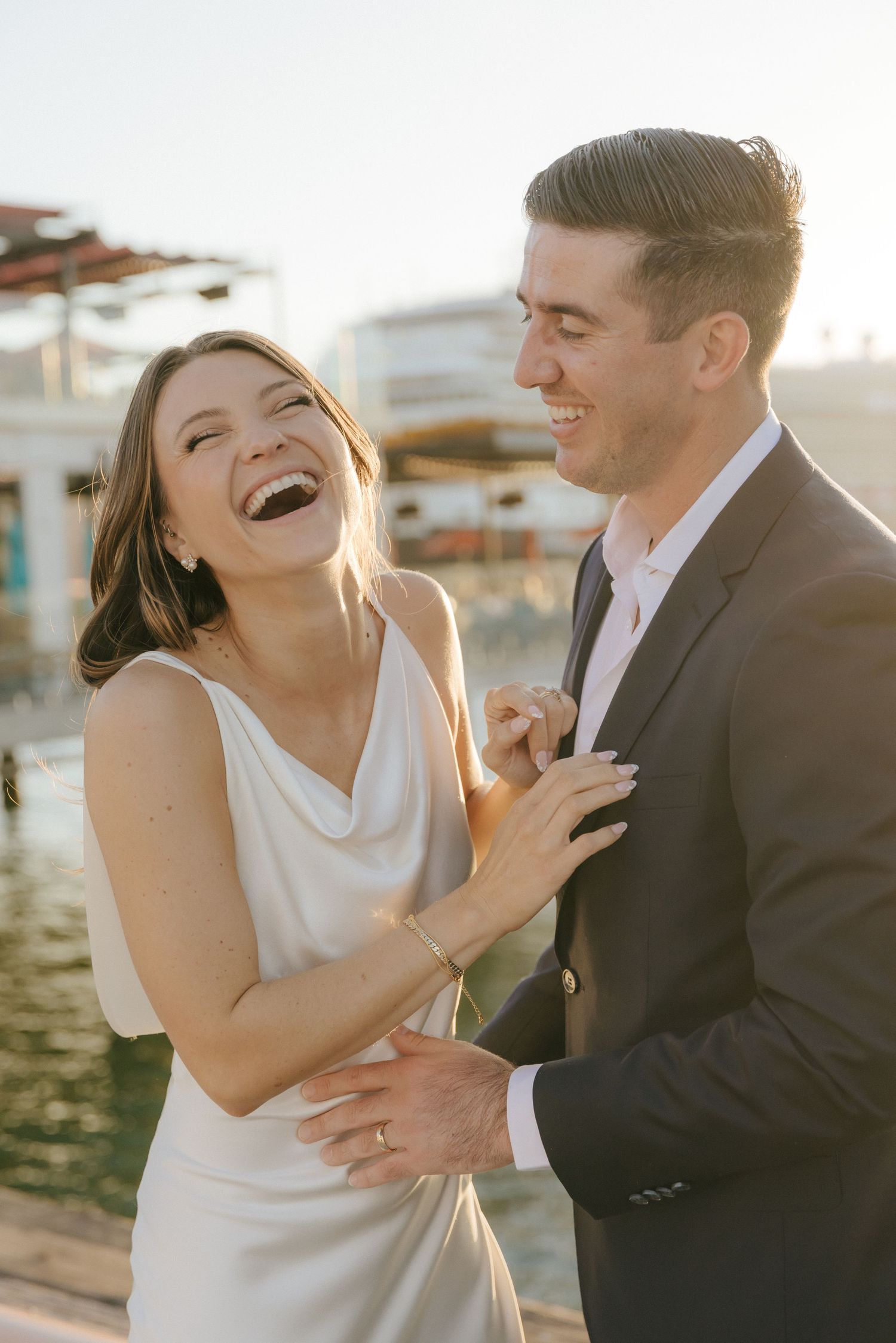 A romantic couple shares joyful laughter during their sunset waterfront photo session.