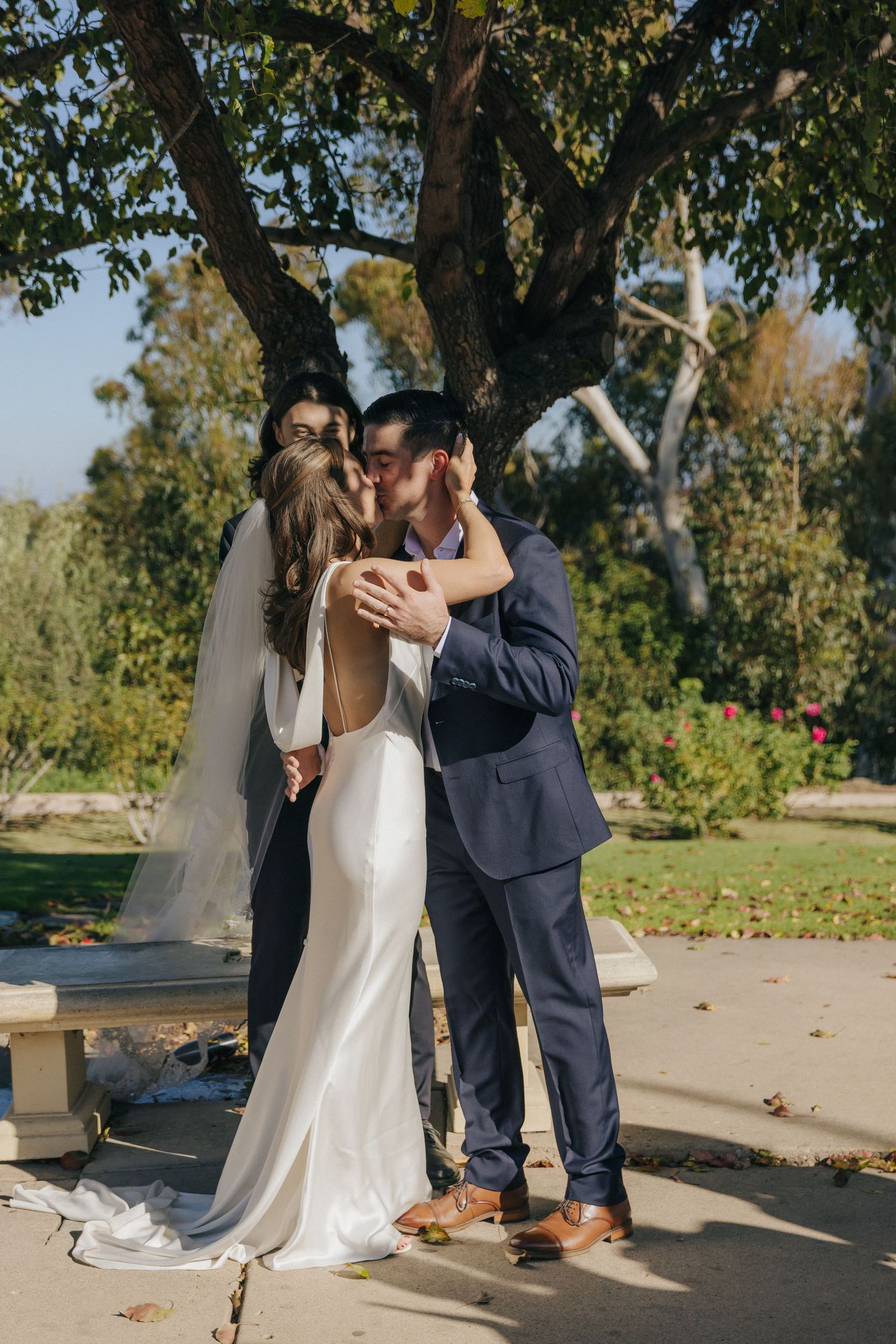 A romantic wedding couple shares intimate moments in a garden setting with natural sunlight.