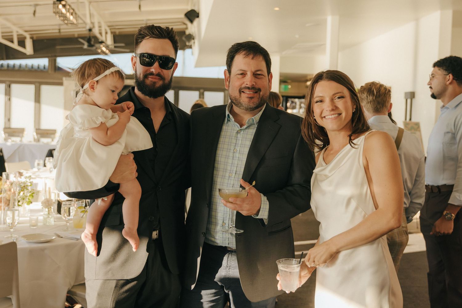Wedding guests mingle and celebrate during a reception at a bright indoor venue with natural lighting.