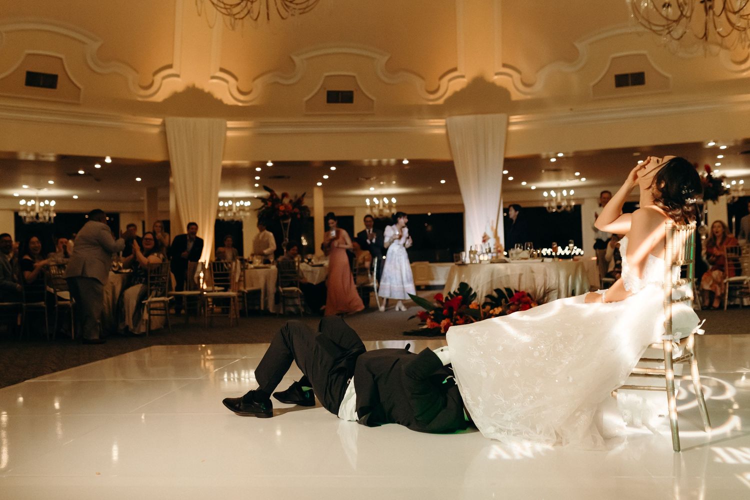 Dynamic dance move captured on a glossy ballroom floor under warm lighting and elegant chandeliers.