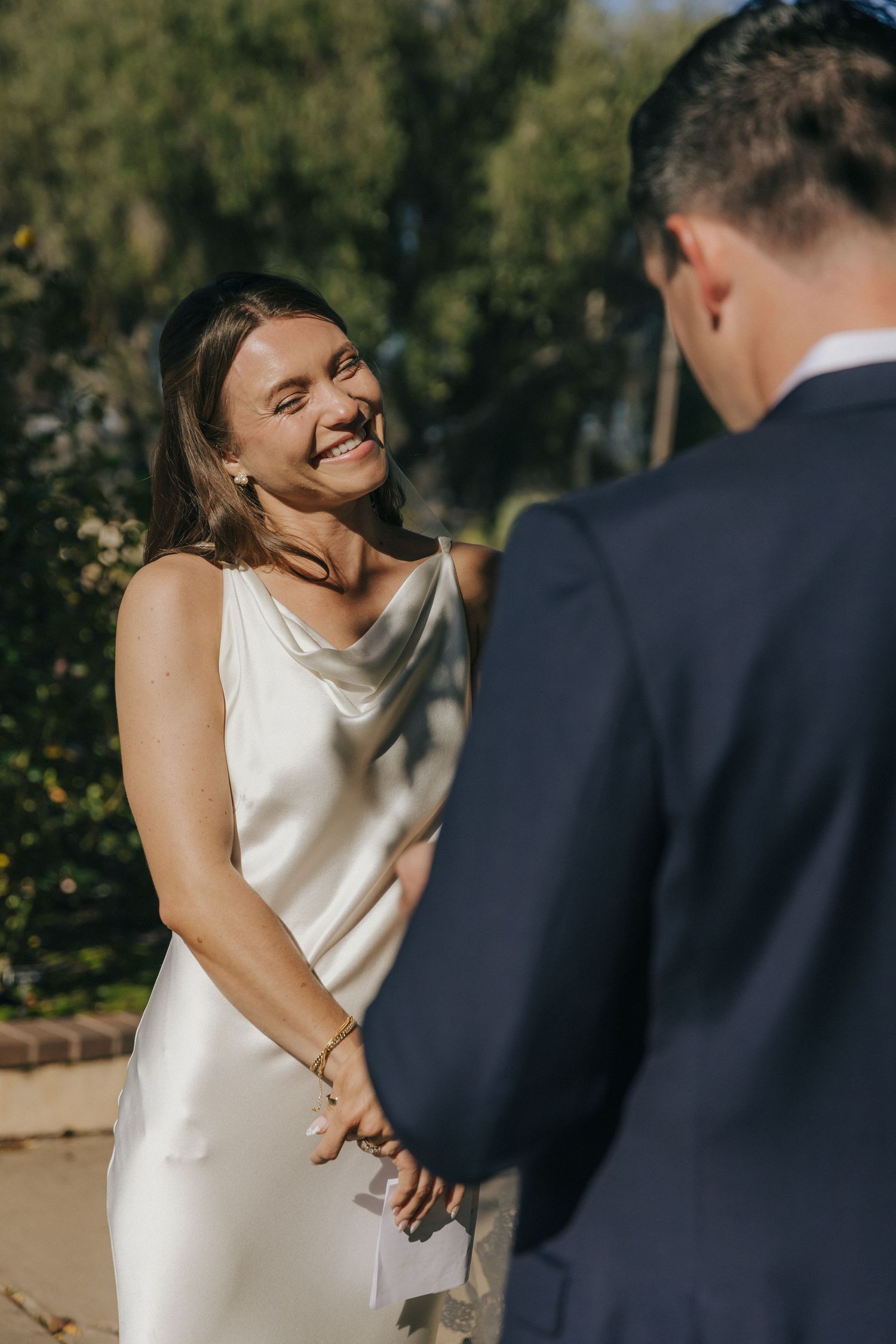 Couple shares a joyful moment during an outdoor wedding photoshoot with natural greenery in the background.