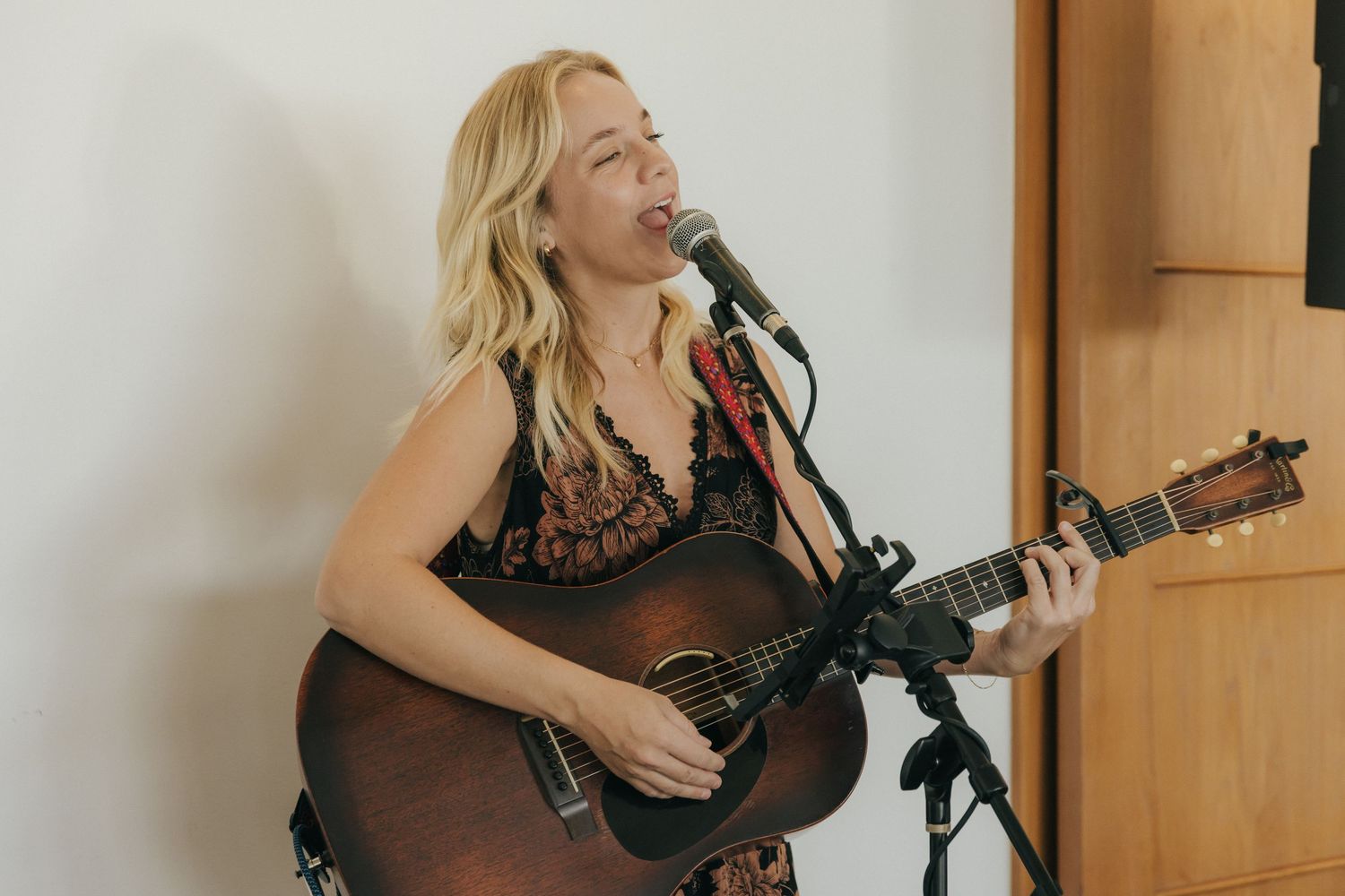 A performer in a black dress plays acoustic guitar and sings into a microphone during a recording session.