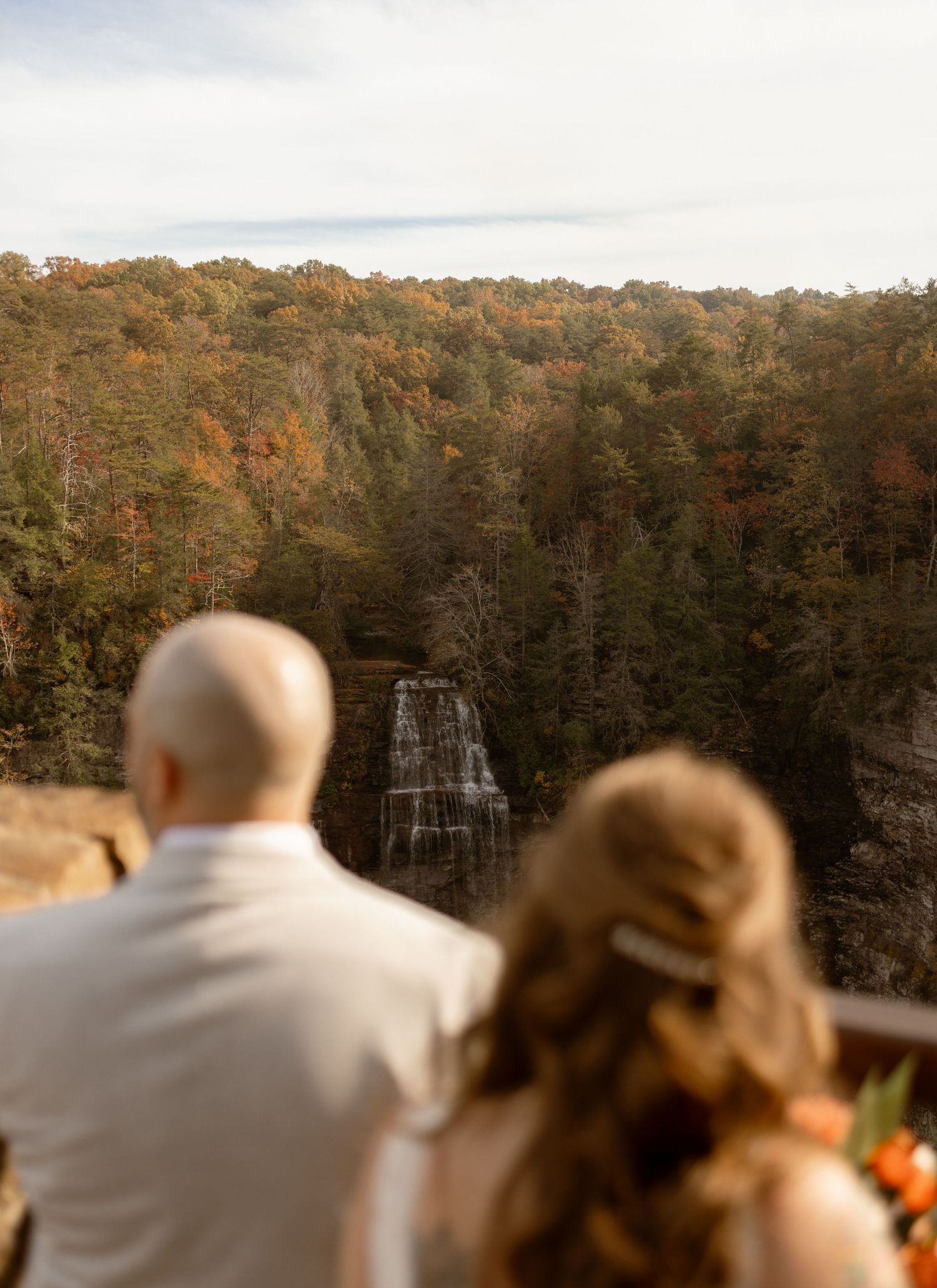 A couple overlooks a stunning waterfall surrounded by colorful autumn foliage from a scenic overlook.