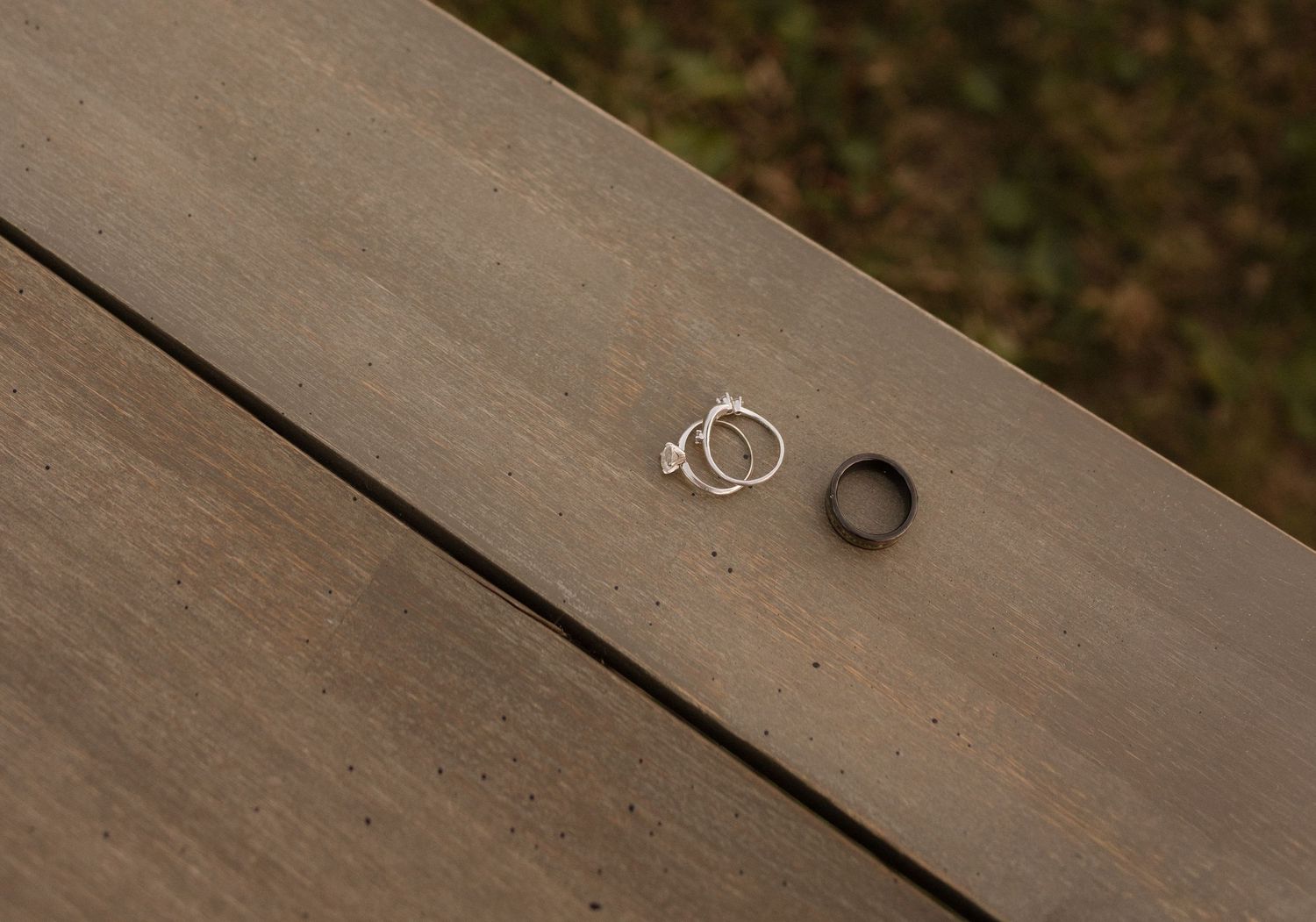 Two silver wedding rings and one black wedding band resting on wooden surface.