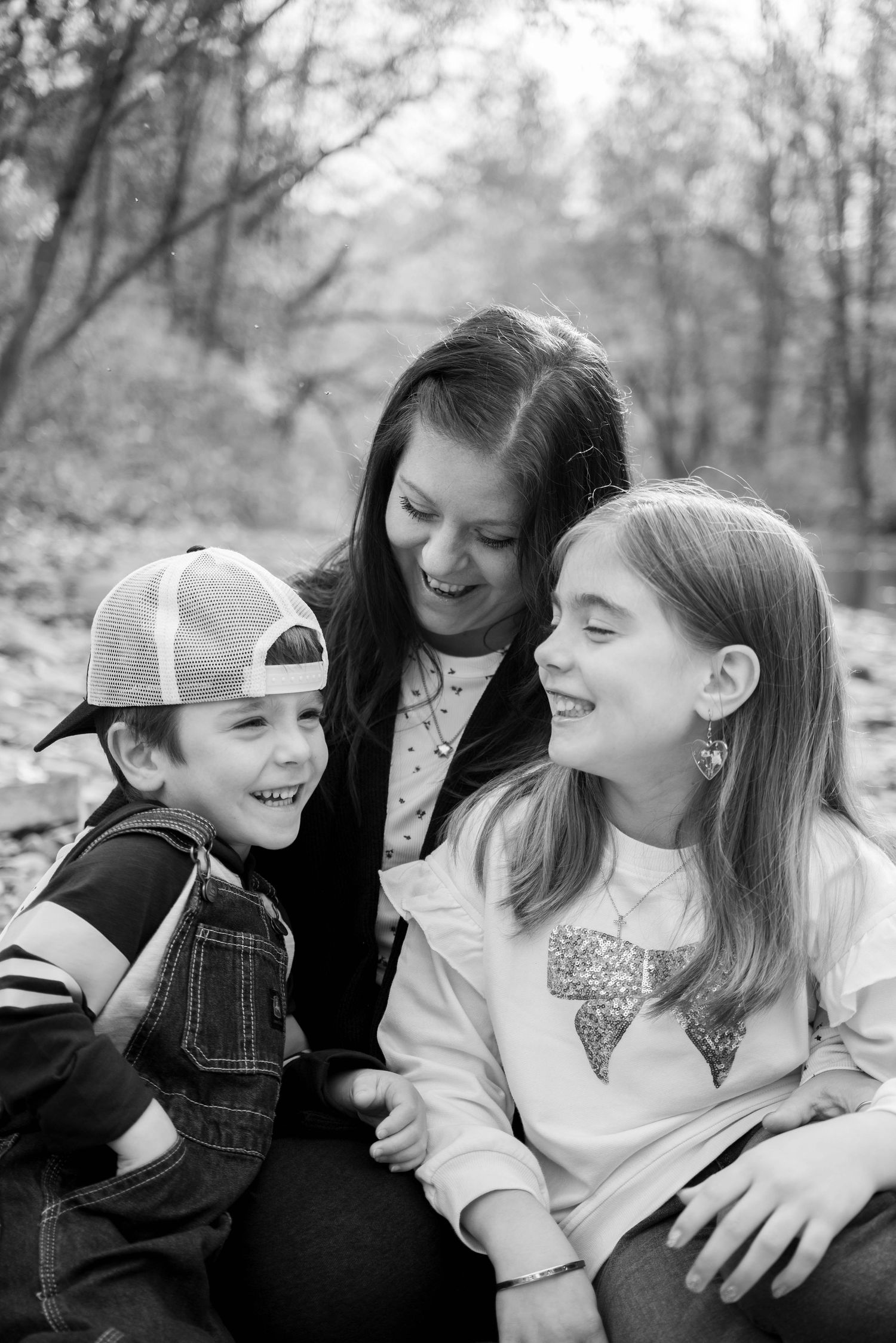 Black and white photo of mother and two children laughing together outdoors in fall.