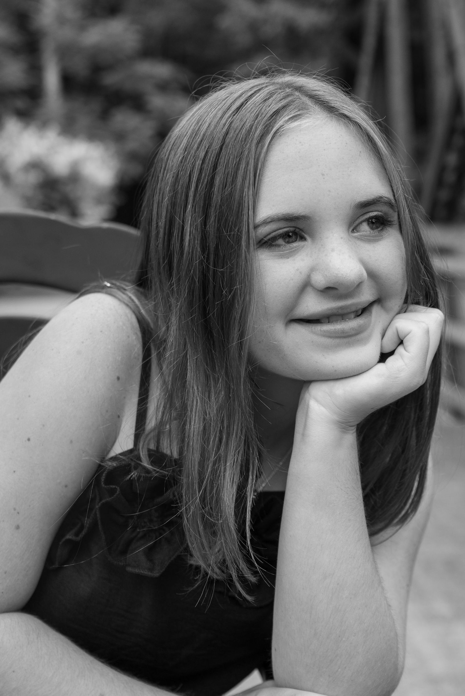 Black and white portrait of a smiling young woman resting her chin on her hand outdoors.