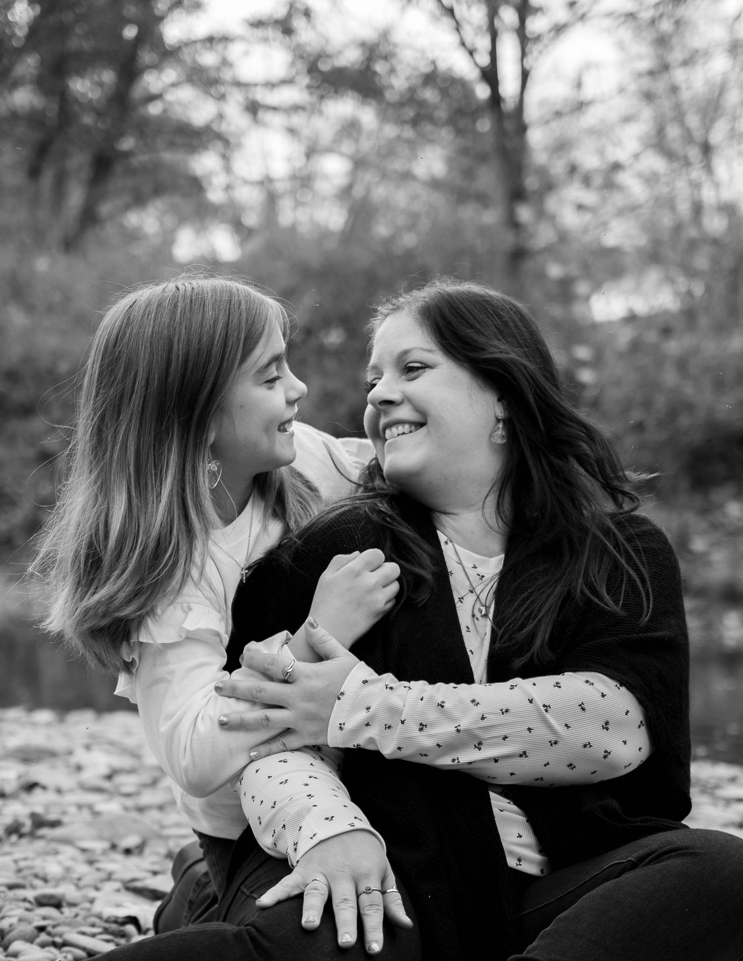 A woman and young girl share a joyful moment together outdoors in a black and white portrait.