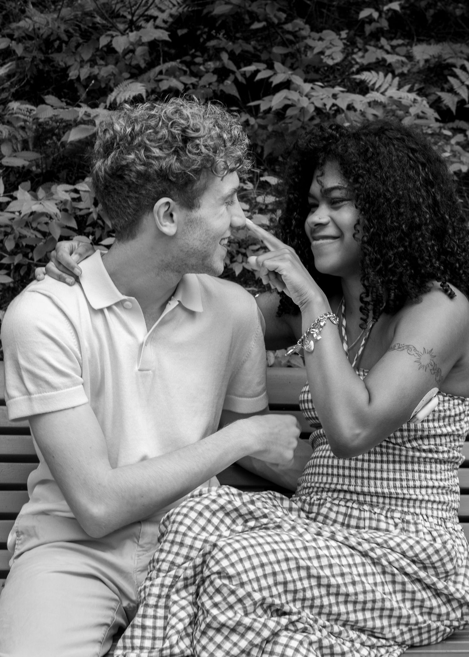 Black and white photo of a happy couple sitting on a bench, smiling at each other outdoors.
