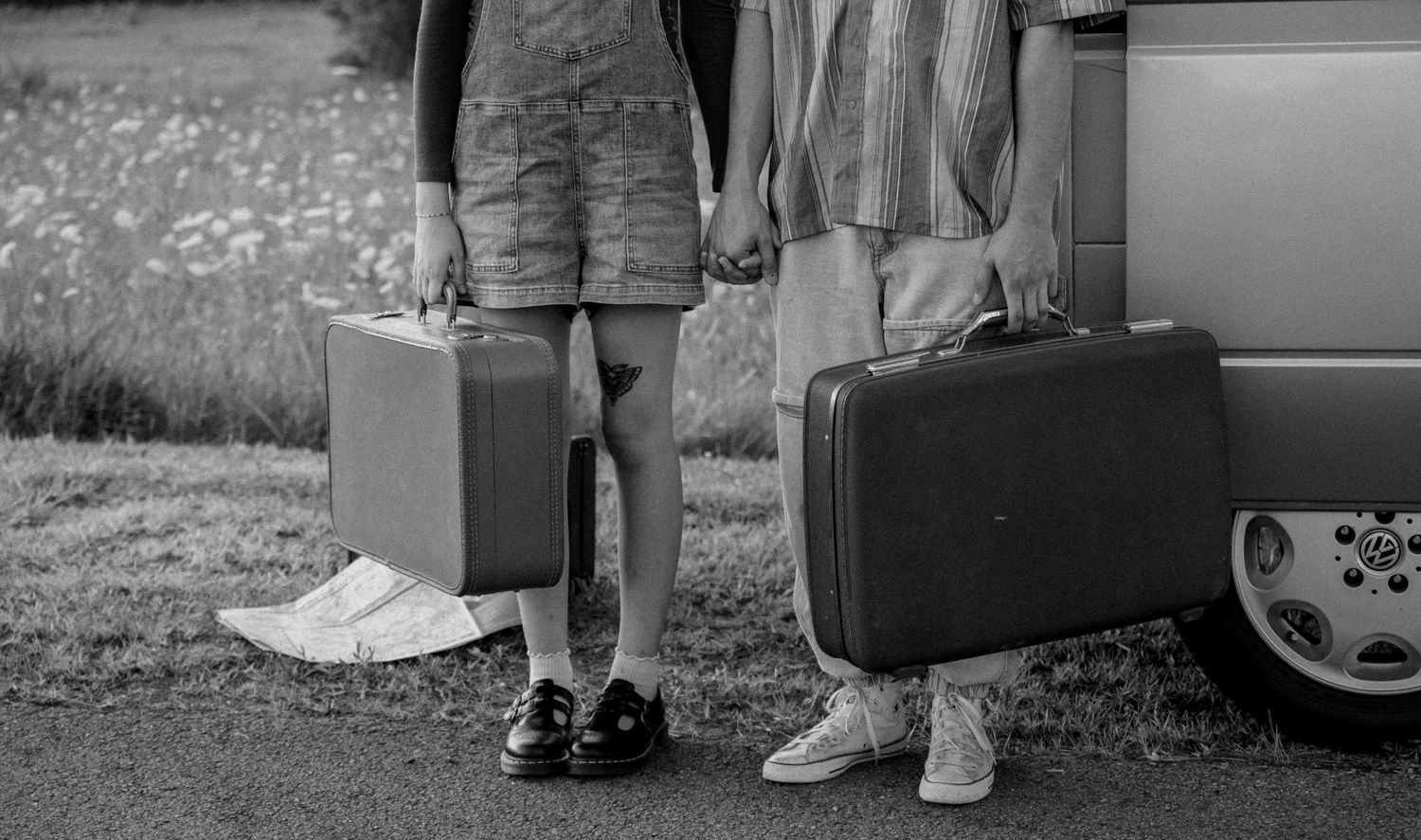 Two people holding vintage suitcases stand beside a car, captured in black and white, ready for a road trip.