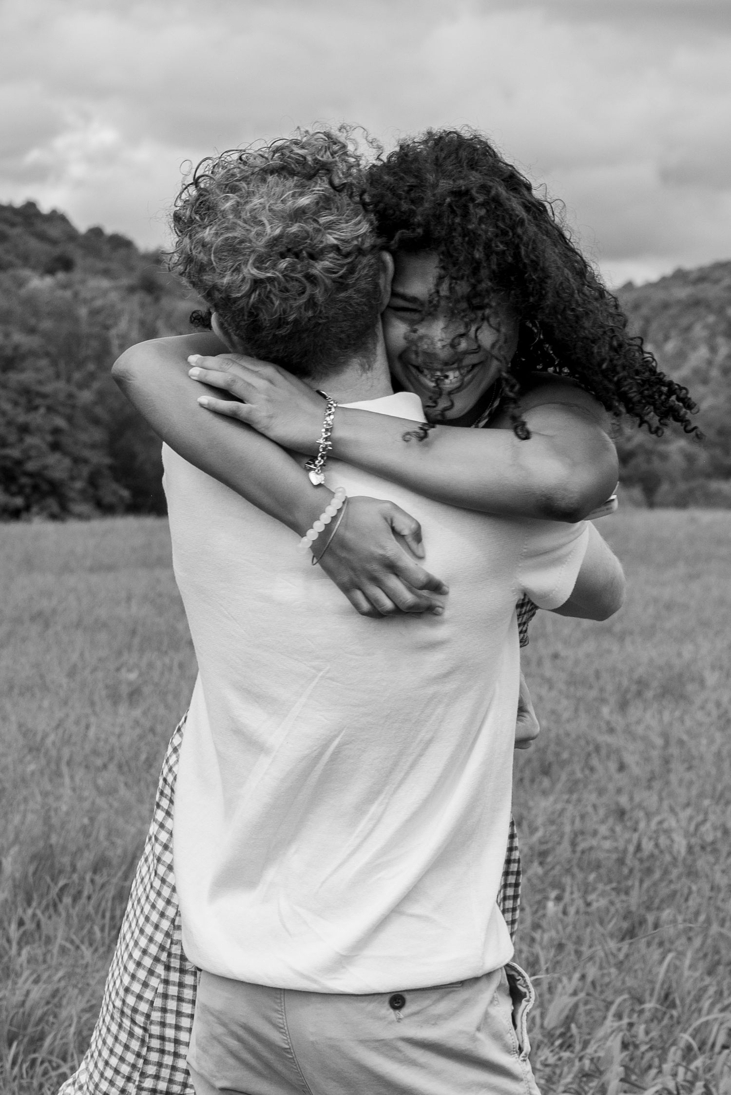 Black and white photo of an interracial couple embracing in a field, smiling and hugging outdoors.