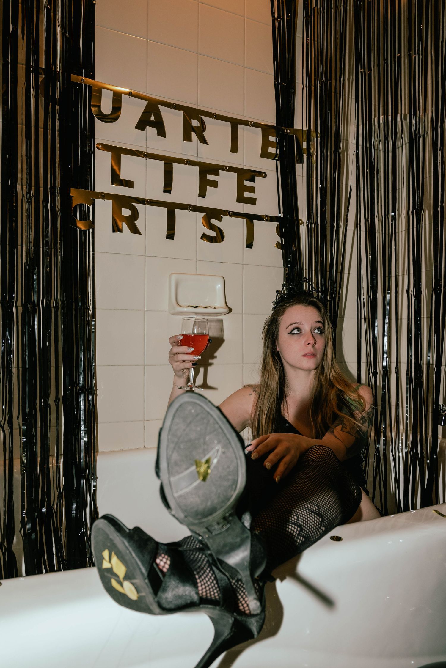 Woman sitting in bathtub holding wine glass with Quarter Life Crisis banner and black streamers.