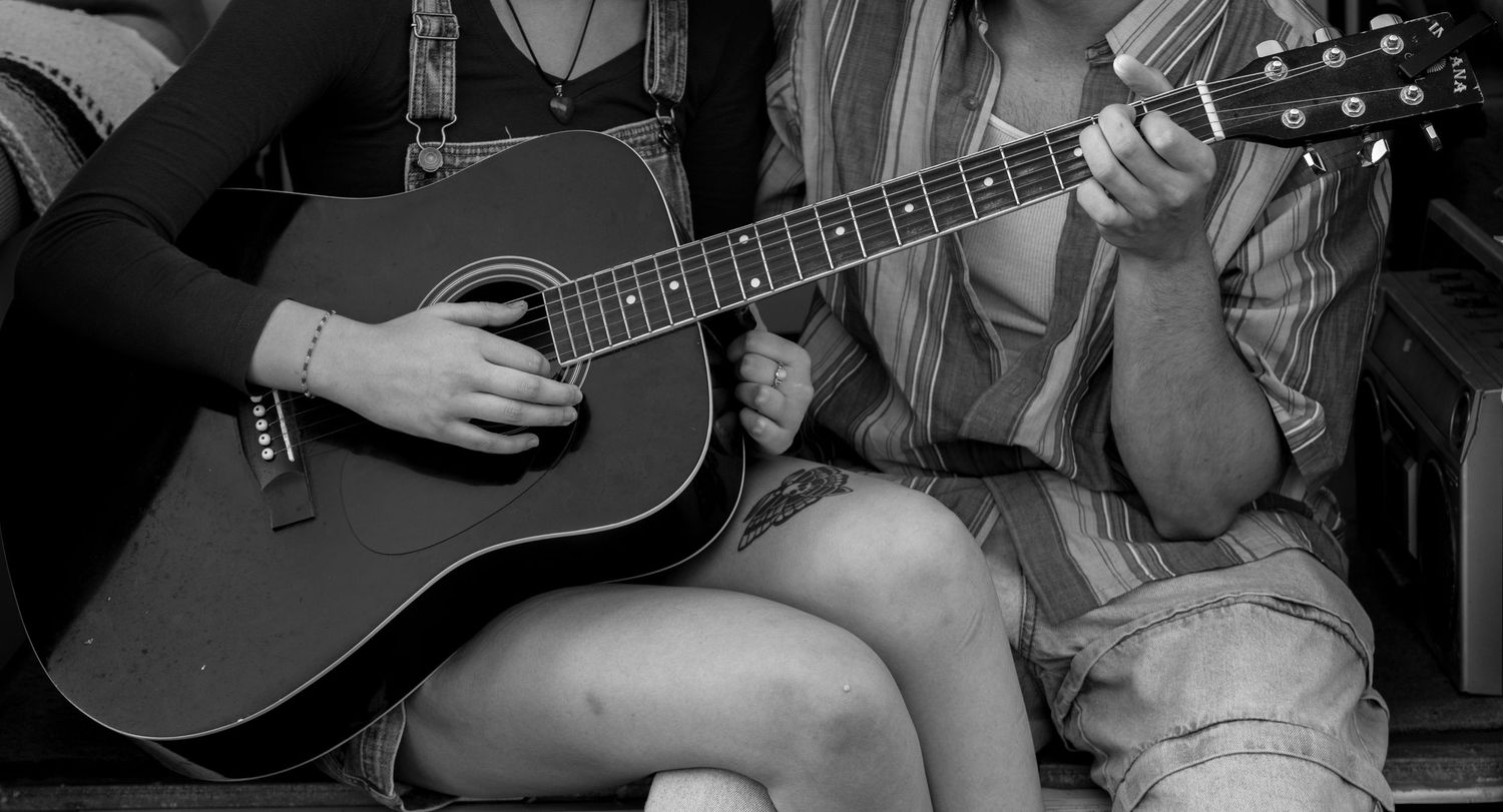 Two people playing acoustic guitar together in black and white photo.