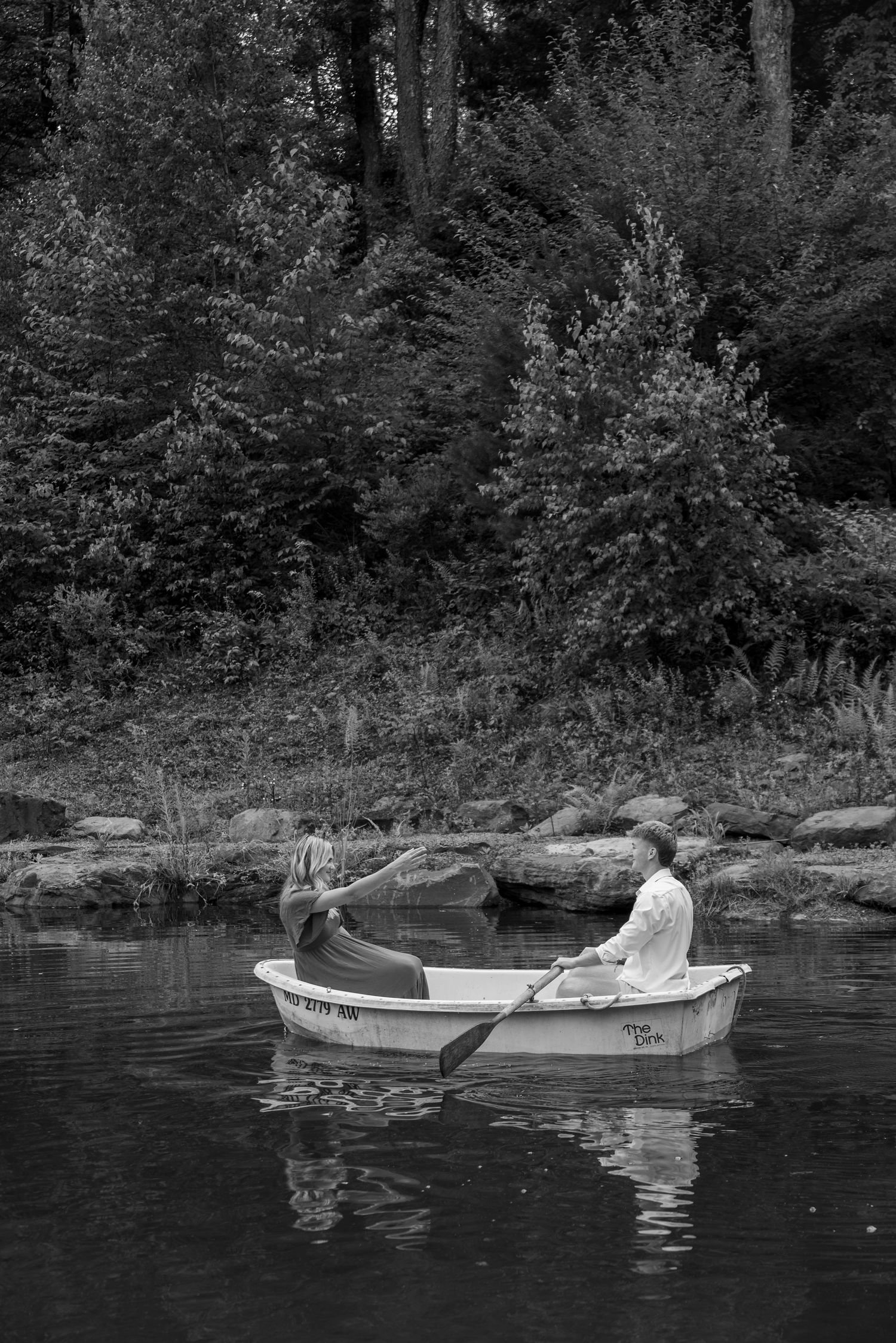 Couple rowing a small boat on a calm lake surrounded by trees in a romantic black and white outdoor photo.