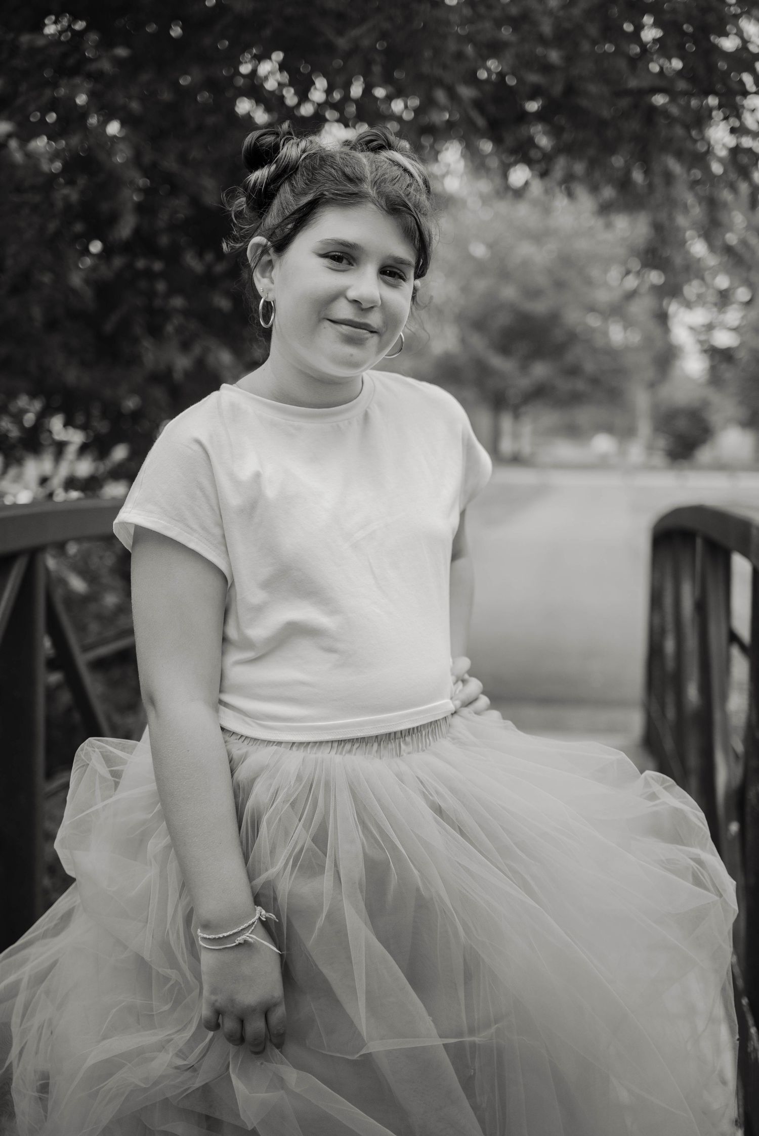 Black and white portrait of a young girl in white tee and tulle skirt sitting on a bridge.